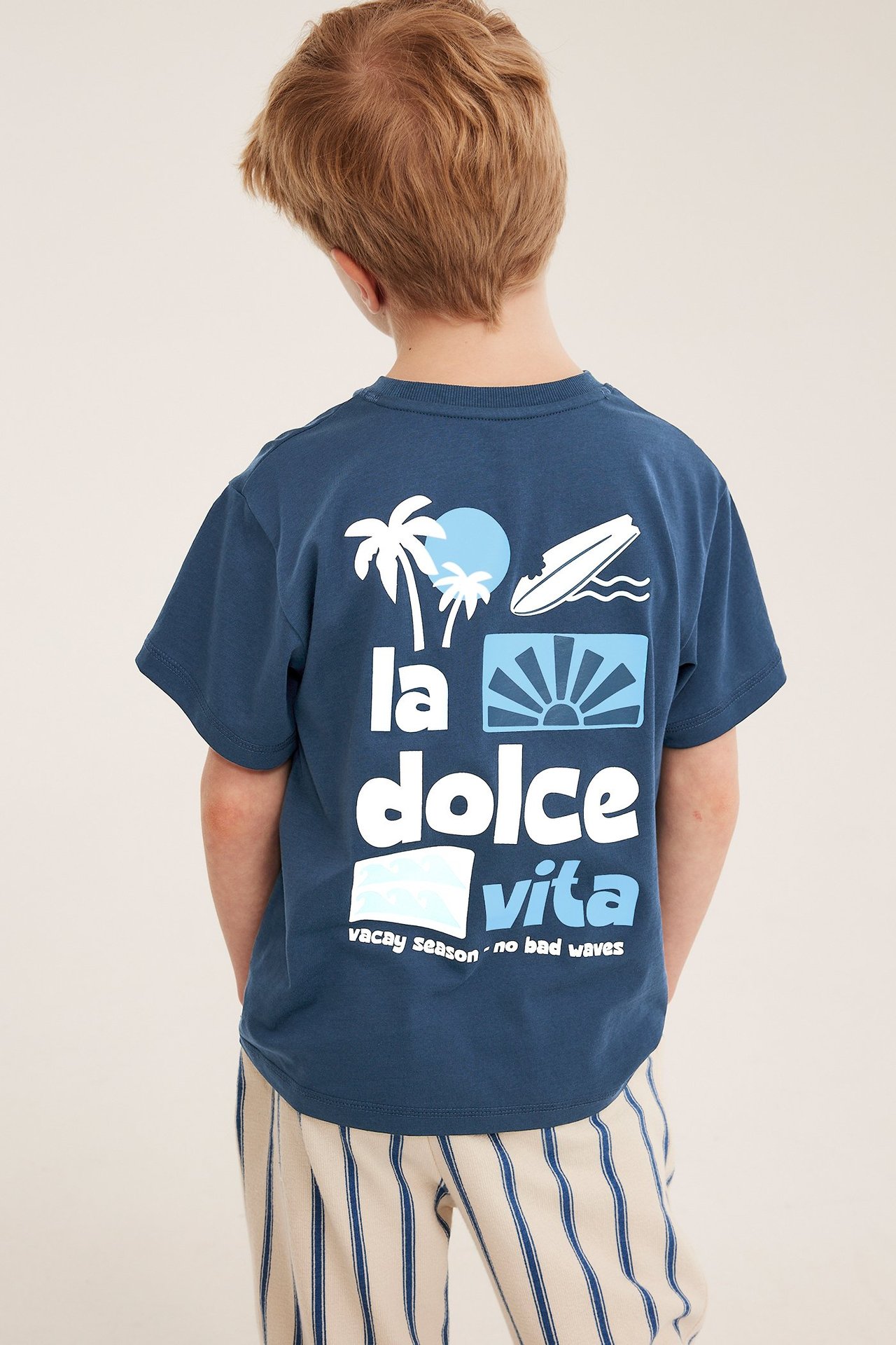 Bakfra, barn i blå bomulls oversize t-skjorte med teksttrykk og stripete bukser.