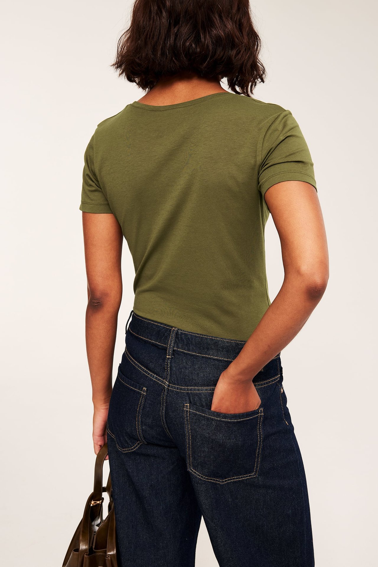 Ryggvy: Kvinna i grön t-shirt, mörkblå jeans och med en brun handväska.