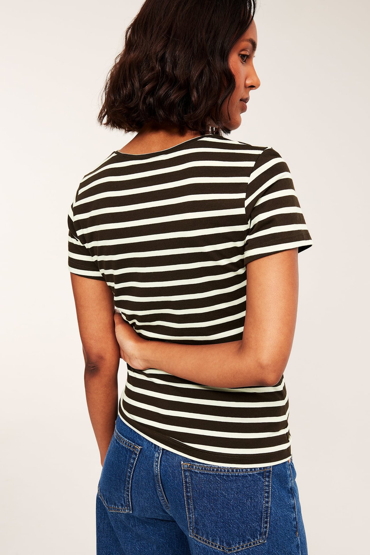 Bakifrån: kvinnas figurnära mörkgröna och vitrandiga kortärmad t-shirt och blå jeans.