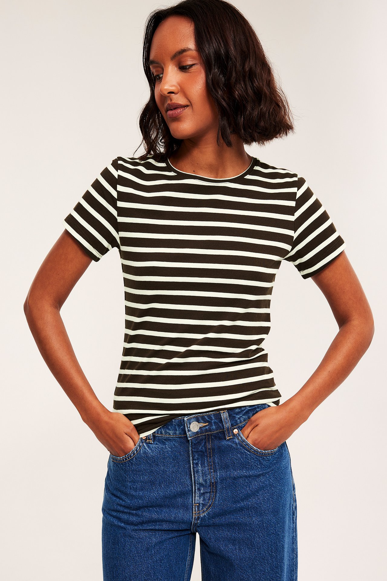 Framifrån: kvinna i mörkgrön och vitrandig kortärmad t-shirt och blå jeans.