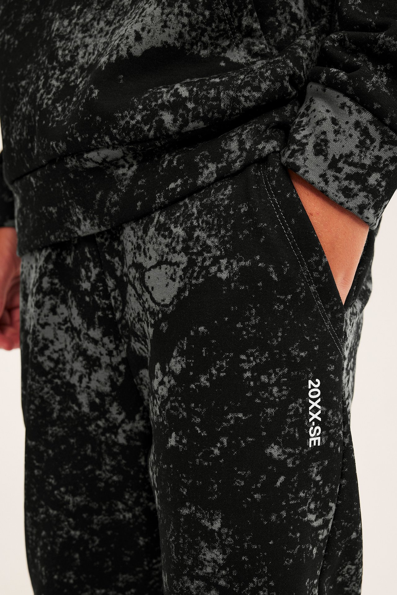 Närbild av vuxen man i svarta och gråmönstrade sweatpants med vit text och matchande sweatshirt.