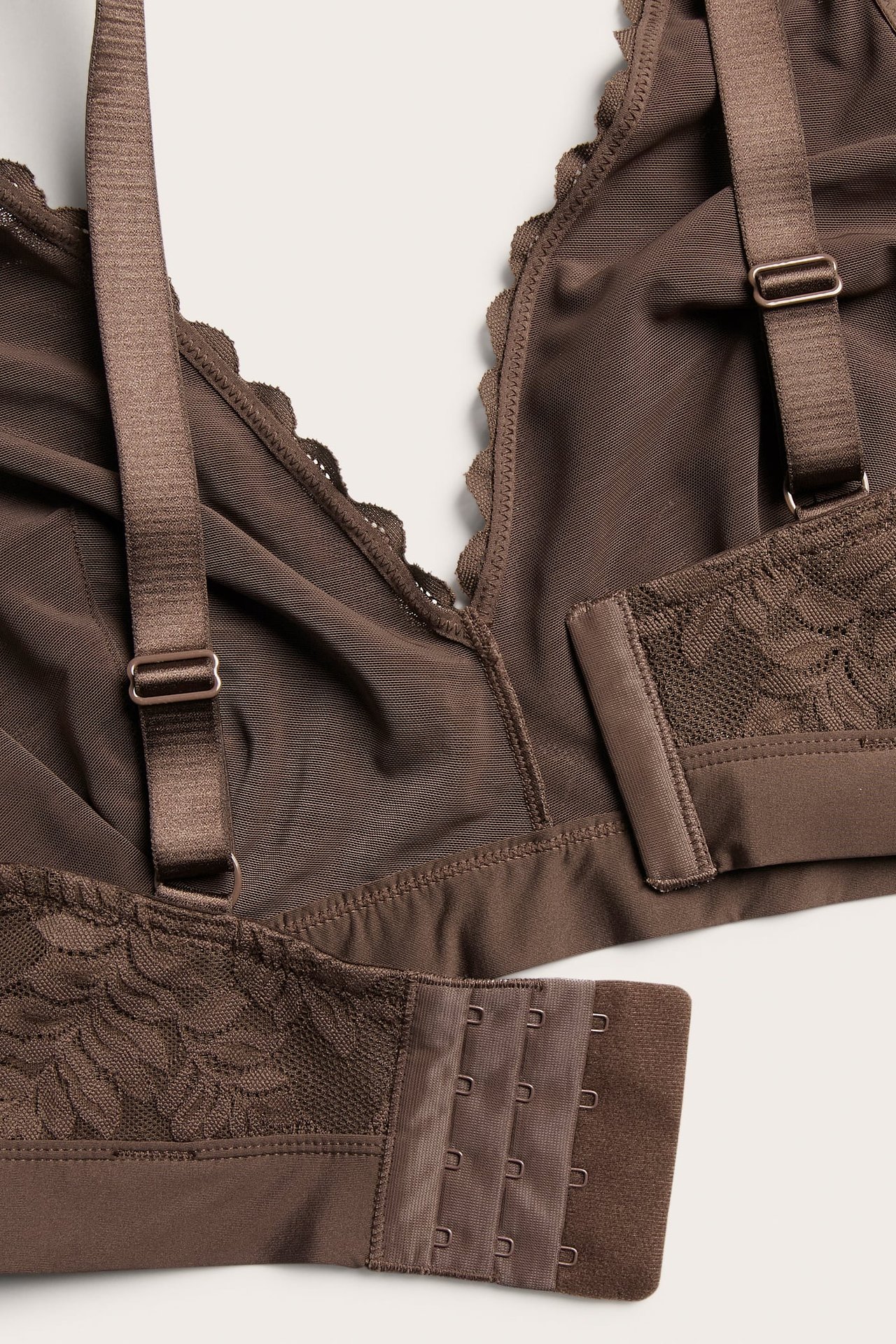 Widok z tyłu ciemnobrązowego koronkowego biustonosza bralette z regulowanymi ramiączkami i haftkami.