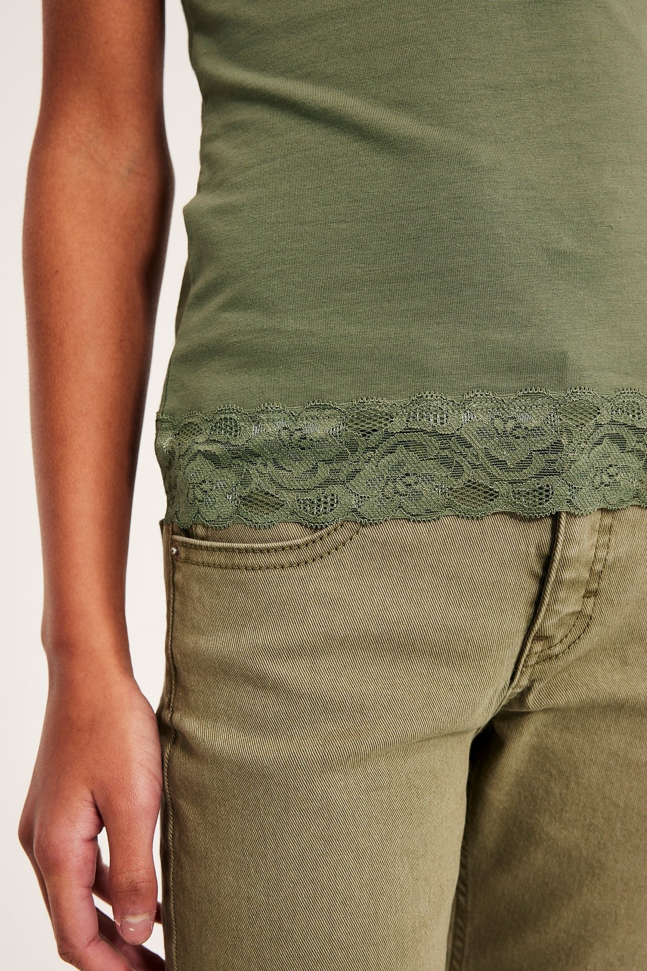 Närbild på ett barn i mörkgrönt trikålinne med spetskant, stylat med olivgröna byxor.