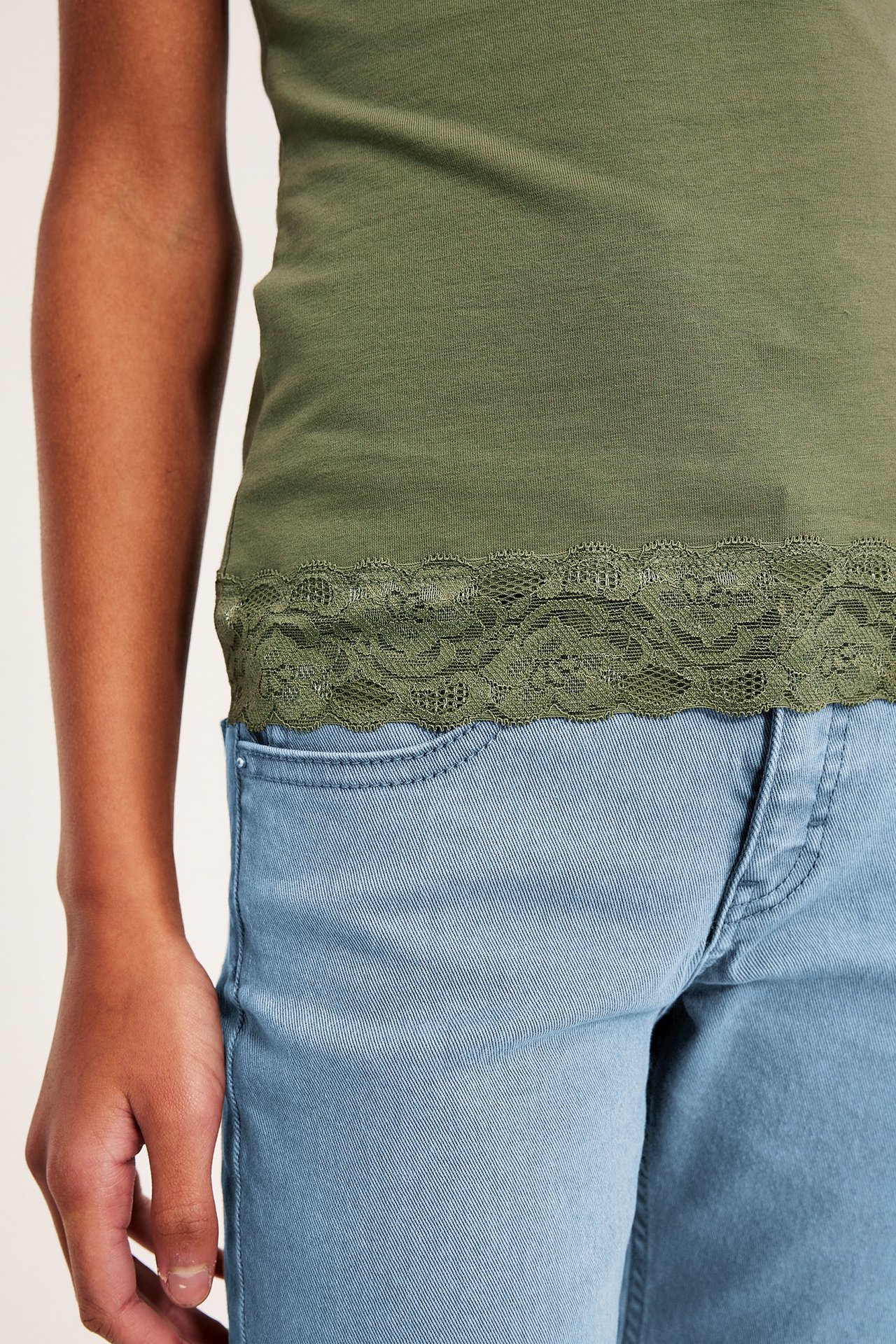 Lähikuva lapsesta tummanvihreässä, istuvassa trikoo topissa pitsireunalla ja vaaleansinisissä farkuissa.