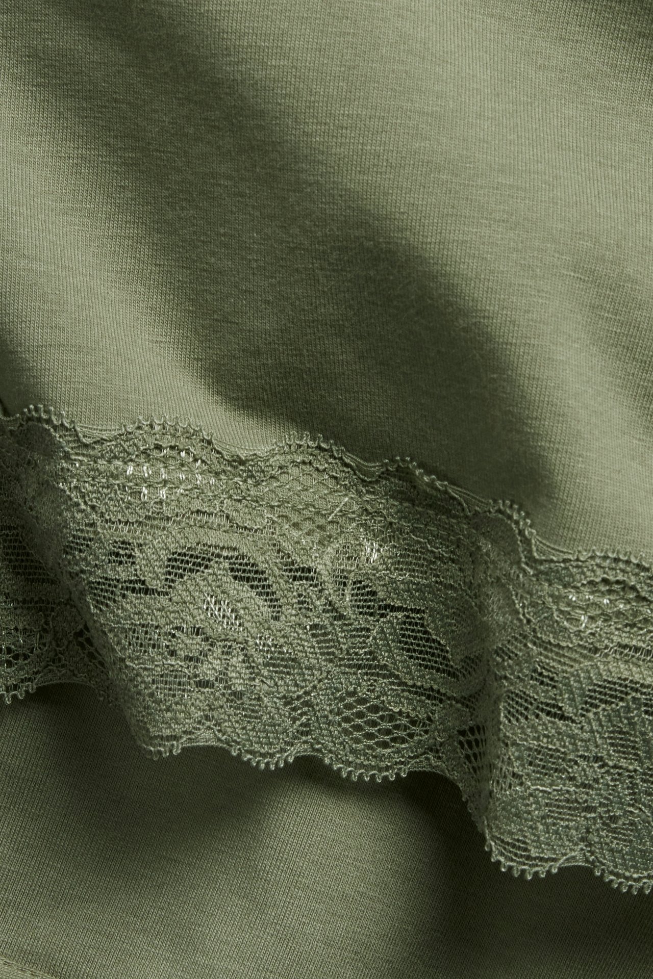 Zbliżenie na ciemnozielony top dzianinowy z ozdobną koronkową lamówką.