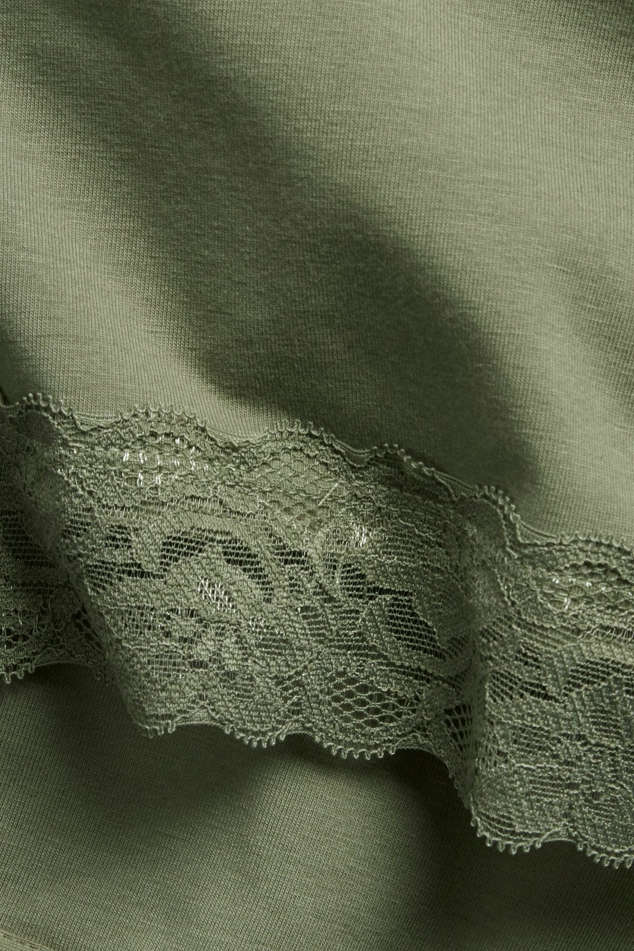 Zbliżenie na ciemnozielony top dzianinowy z ozdobną koronkową lamówką.