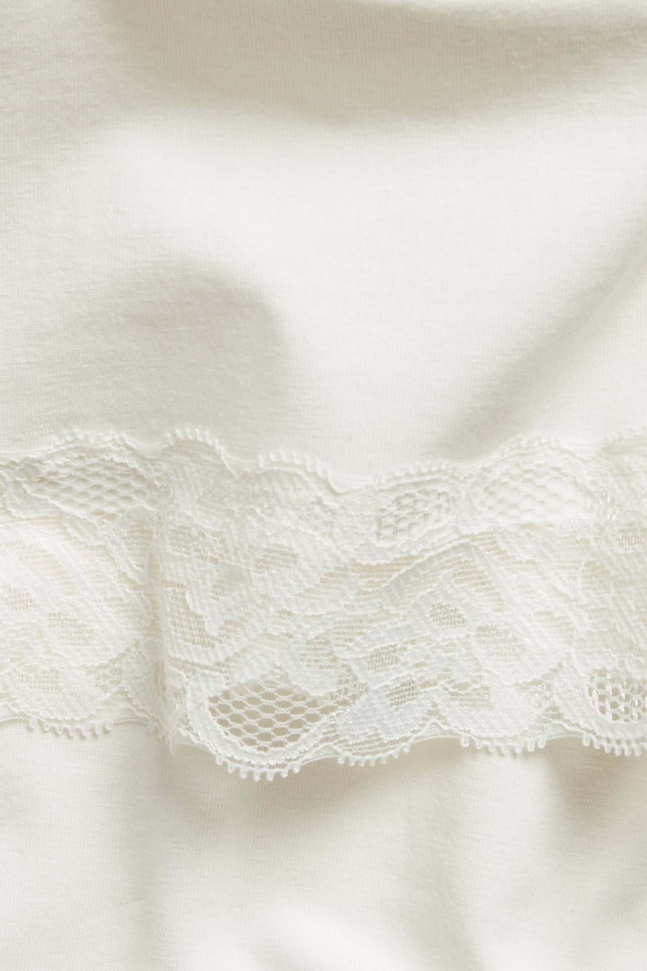 Zbliżenie na kremowy top z dzianiny z ozdobnym koronkowym wykończeniem.