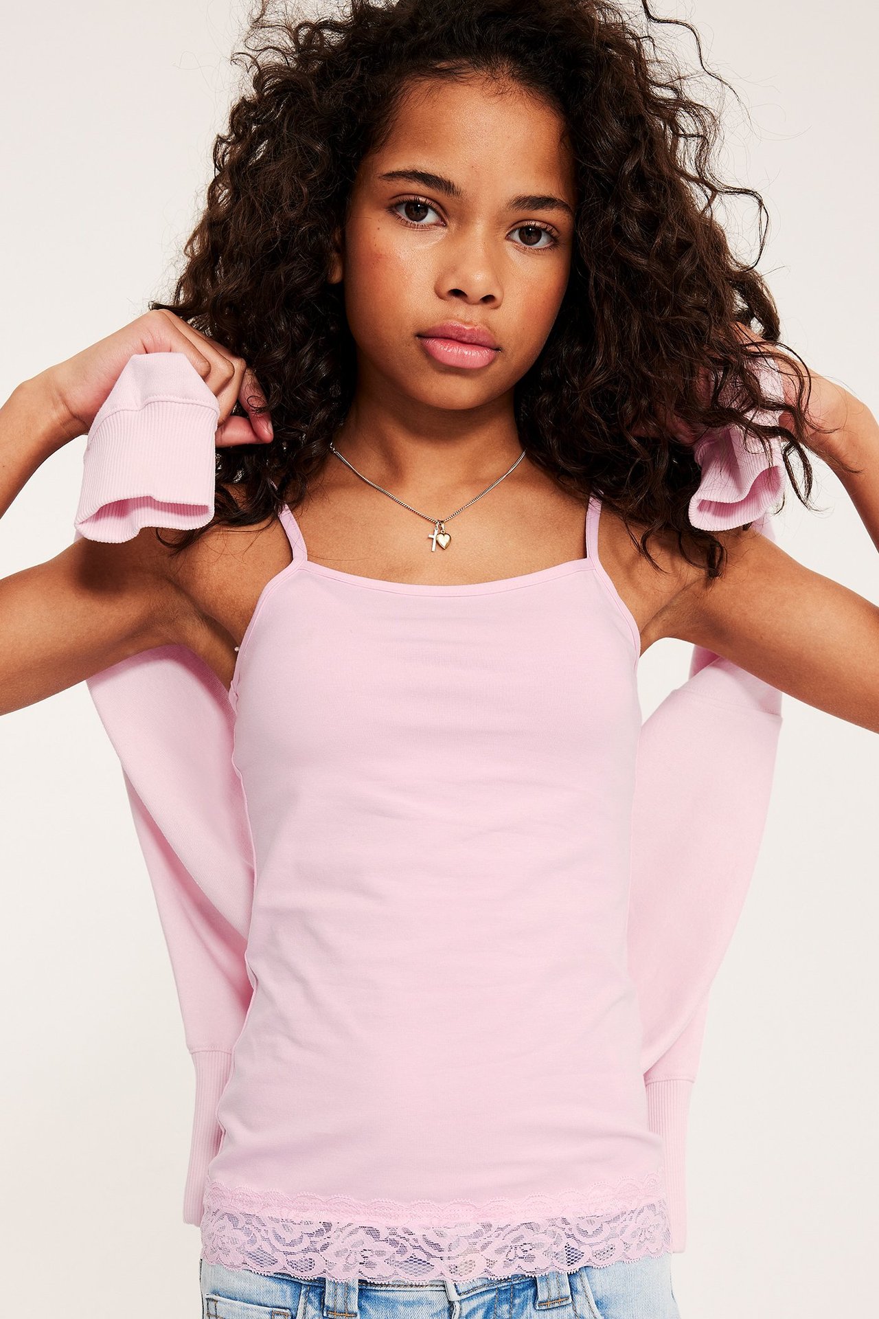 Widok z przodu: Dziecko nosi różowy top na ramiączkach z koronką, jasnoniebieskie dżinsy i srebrny naszyjnik.