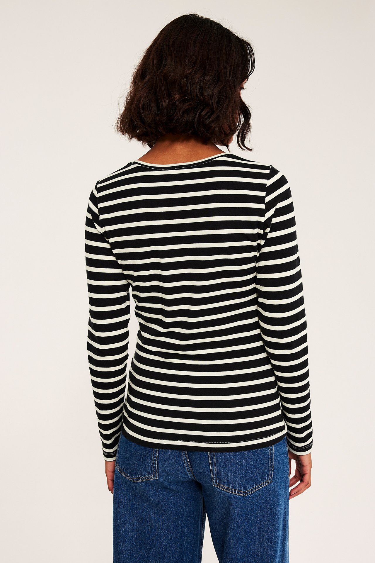 Bakfra, kvinne i svart og hvitstripete langermet topp og blå jeans.