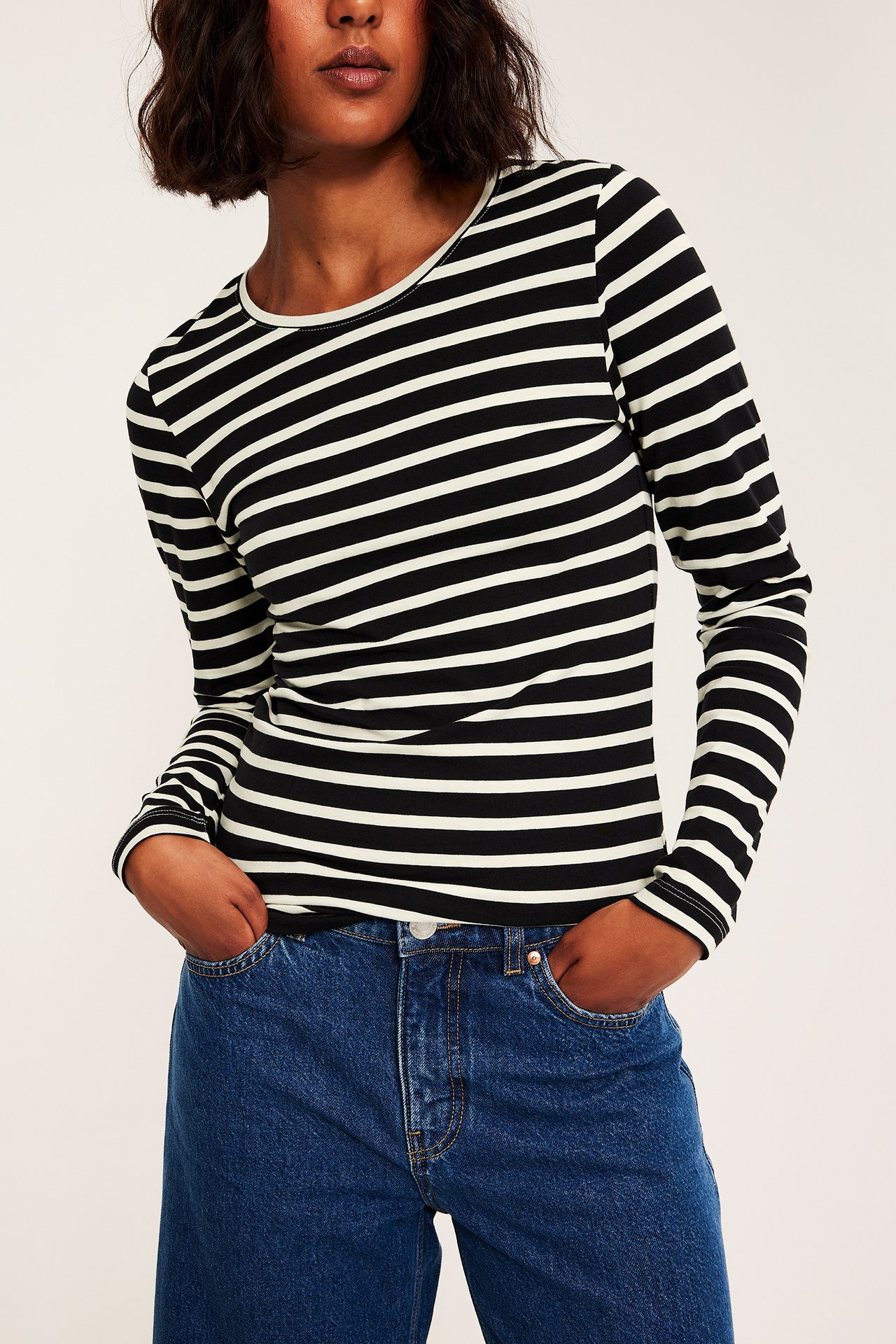 Frontbilde av kvinne i svart- og offwhite-stripet langermet topp og blå jeans.