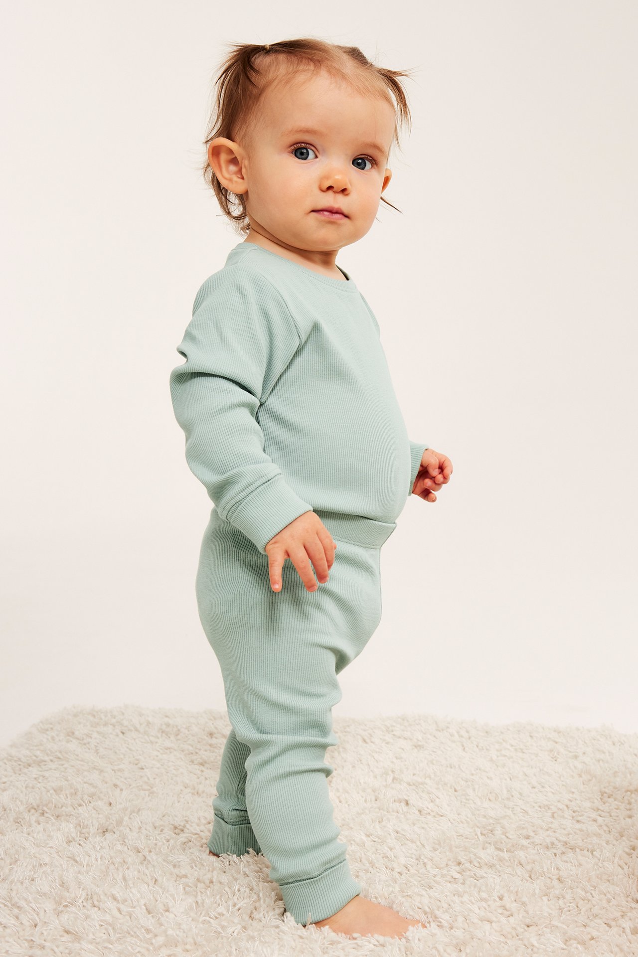 Sidebilde av en baby i en lysegrønn ribbet langermet topp og matchende leggings.