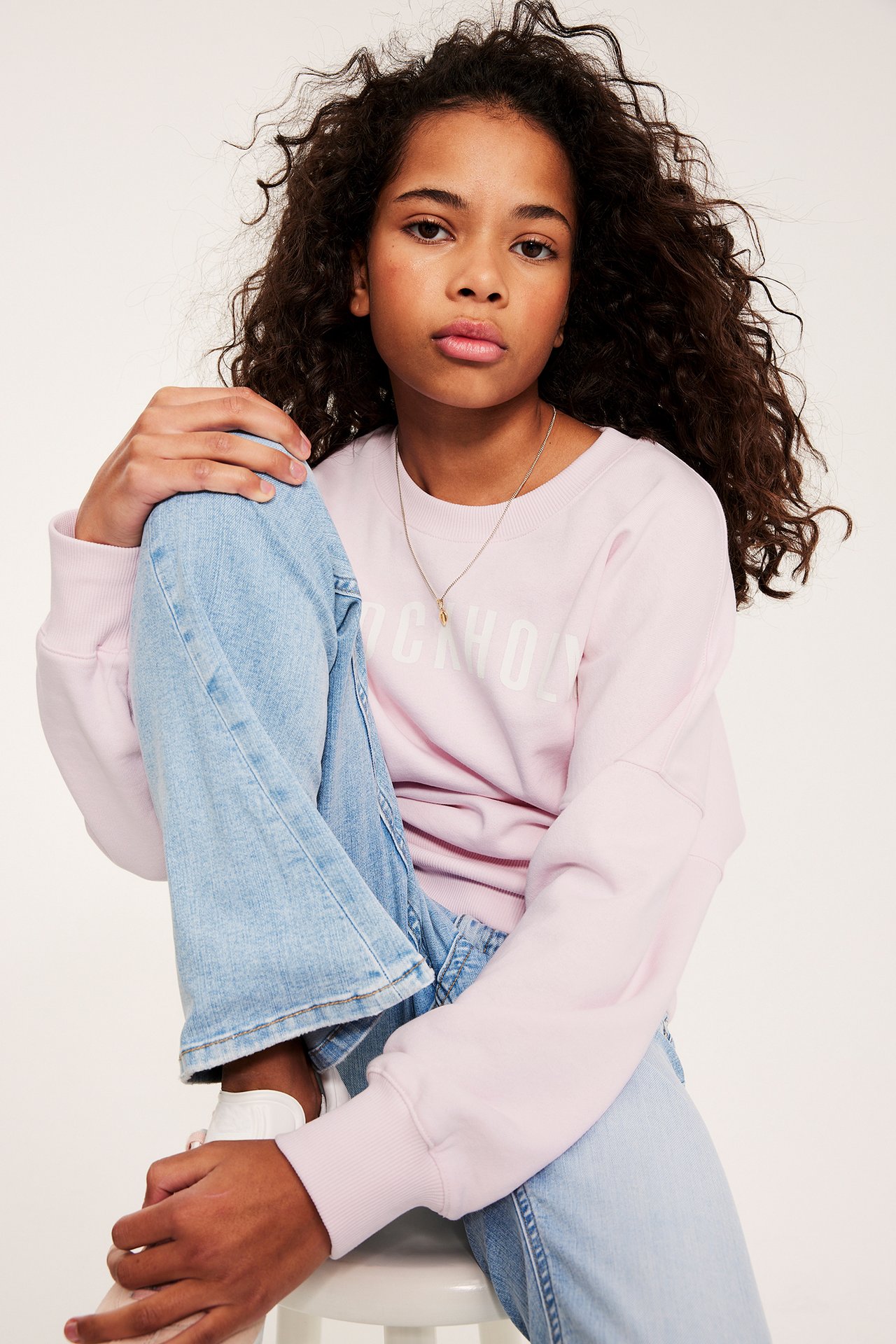 Forfra: et barn i lys rosa 'STOCKHOLM' sweatshirt, lyseblå jeans og hvite sneakers.