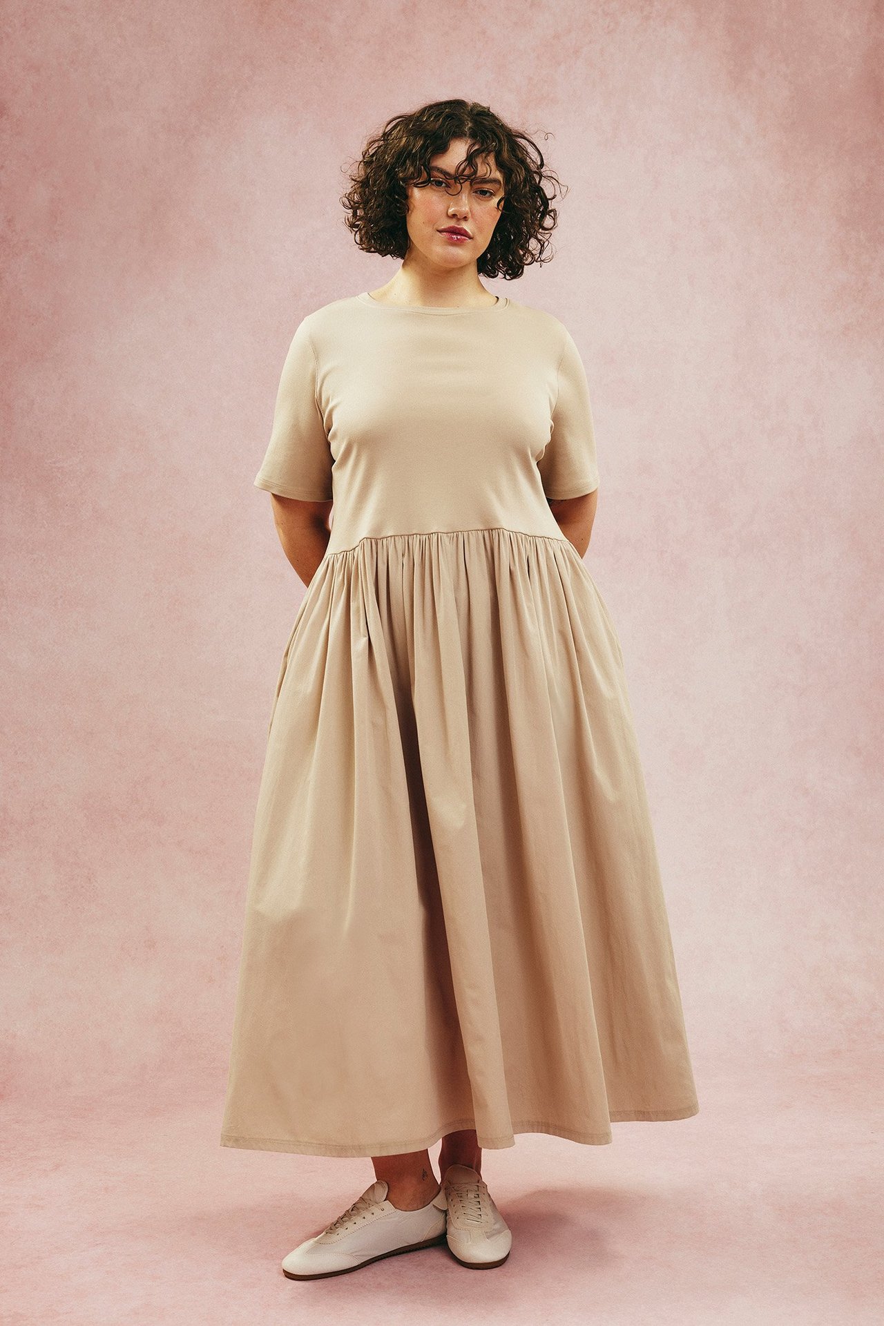 Front: kvinne i beige rundhalset midikjole med jerseytop, poplinskjørt og lyse sneakers.