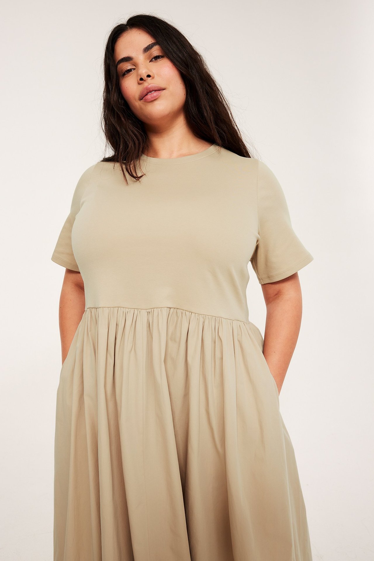 Forfra, kvinne i beige lang kjole med rund hals, korte ermer og rynket skjørt.