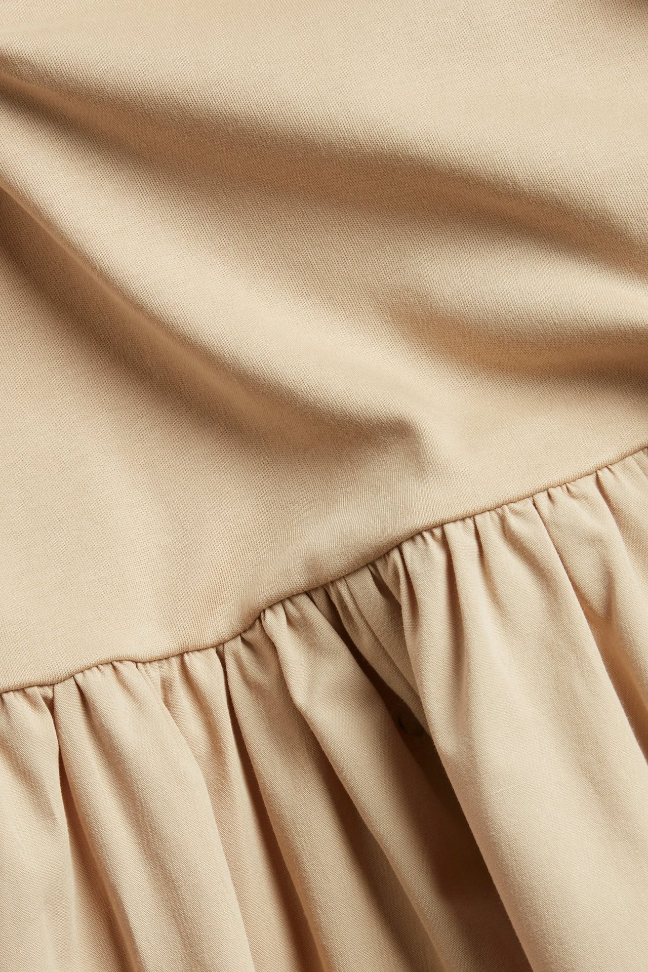 Bliskie ujęcie beżowej sukienki z dzianinową górą i marszczoną spódnicą z bawełnianej popeliny.