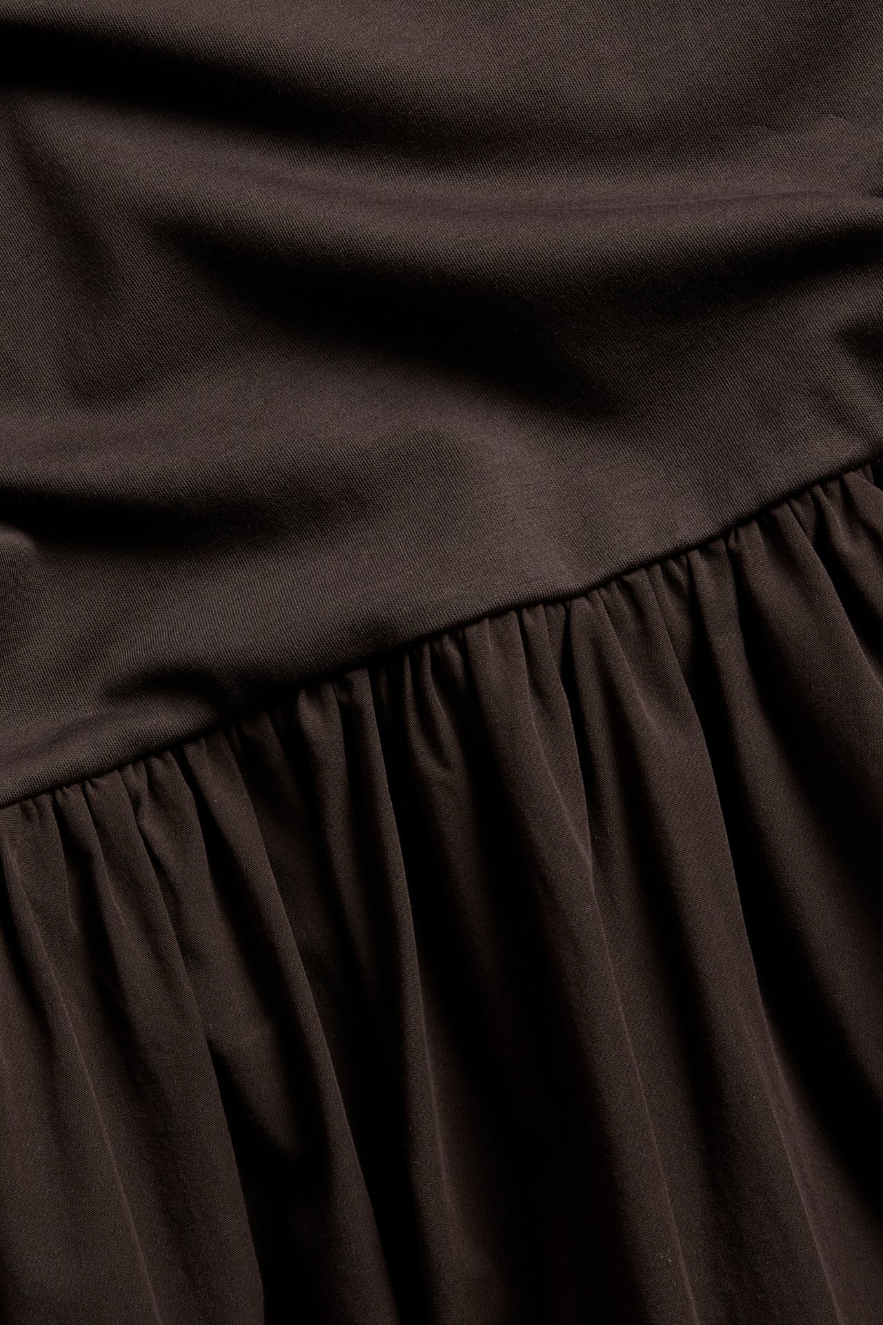 Närbild på mörkbrun klänning med jerseytop och rynkad kjol i bomullspoplin.