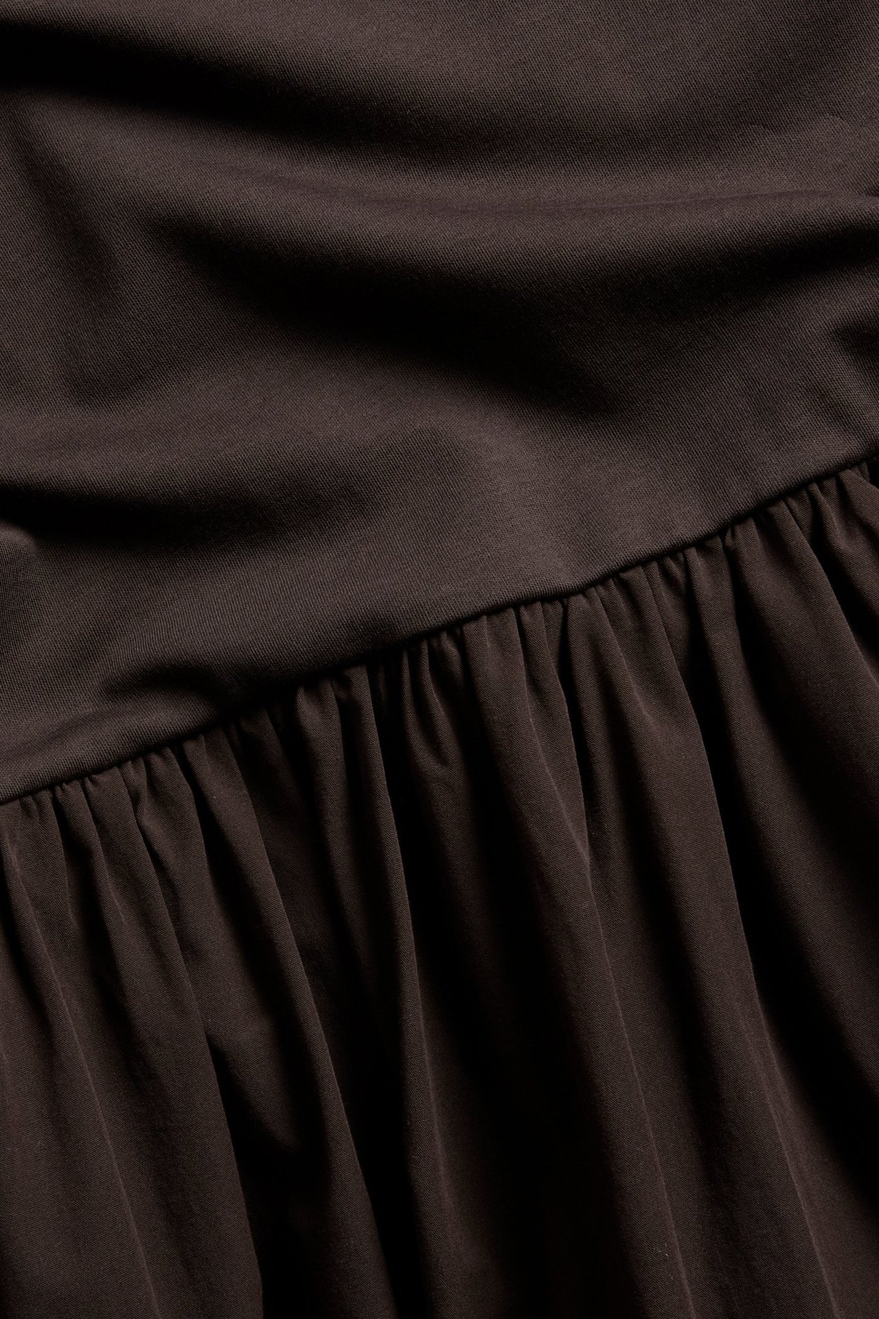 Zbliżenie na ciemnobrązową sukienkę z dżersejową górą i marszczoną bawełnianą spódnicą z popeliny.