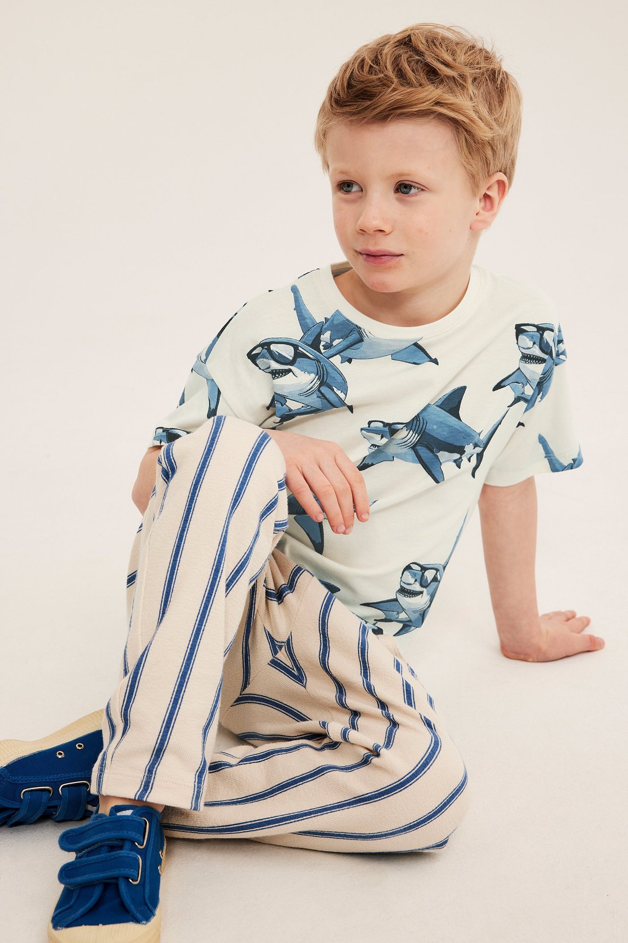 Chłopiec w offwhite T-shircie z wzorem rekinów, normalny krój, opadające ramię, przedni widok.
