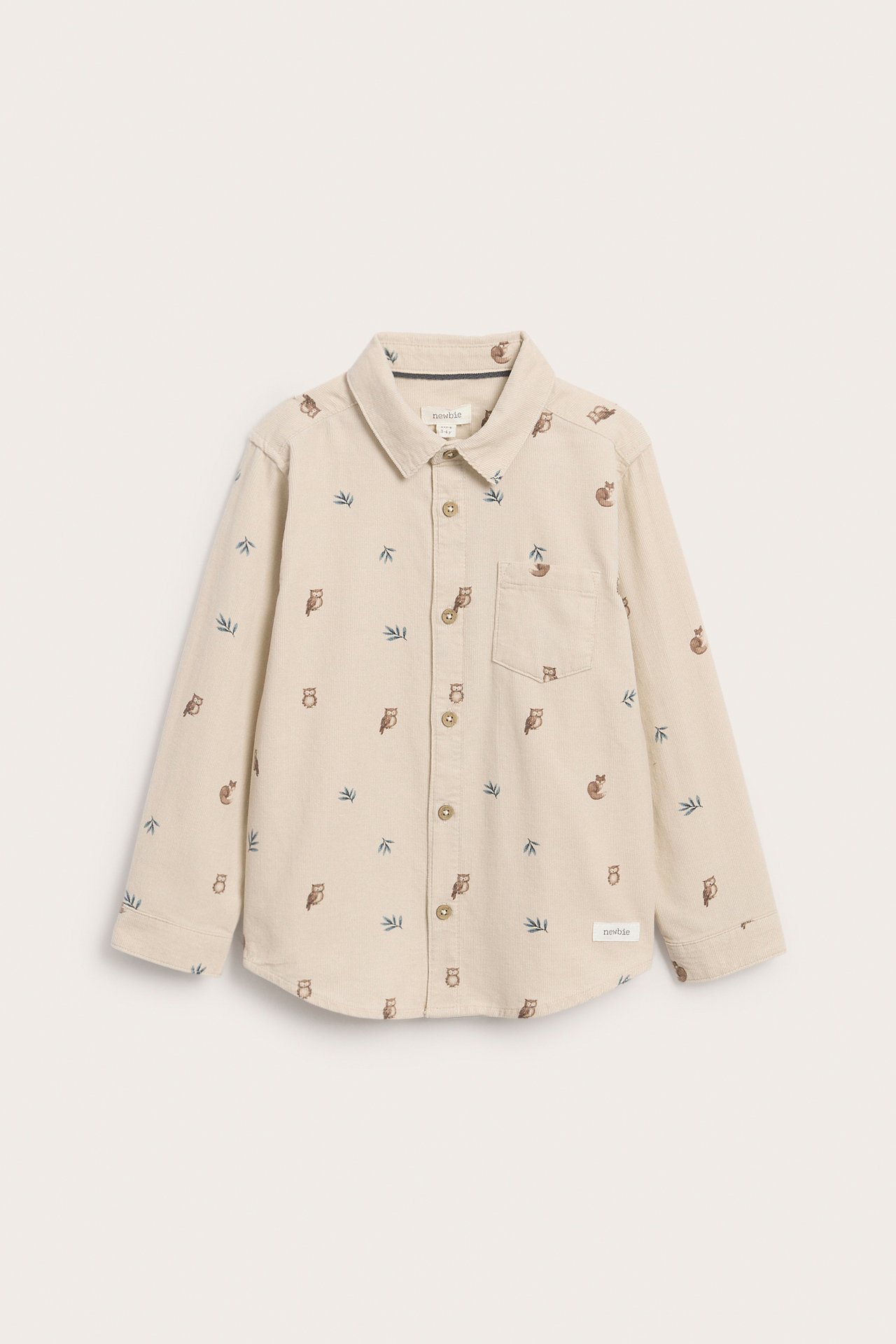 Framifrån, barnskjorta i beige med lång ärm, ugglor och bladmönster, samt knappar fram.