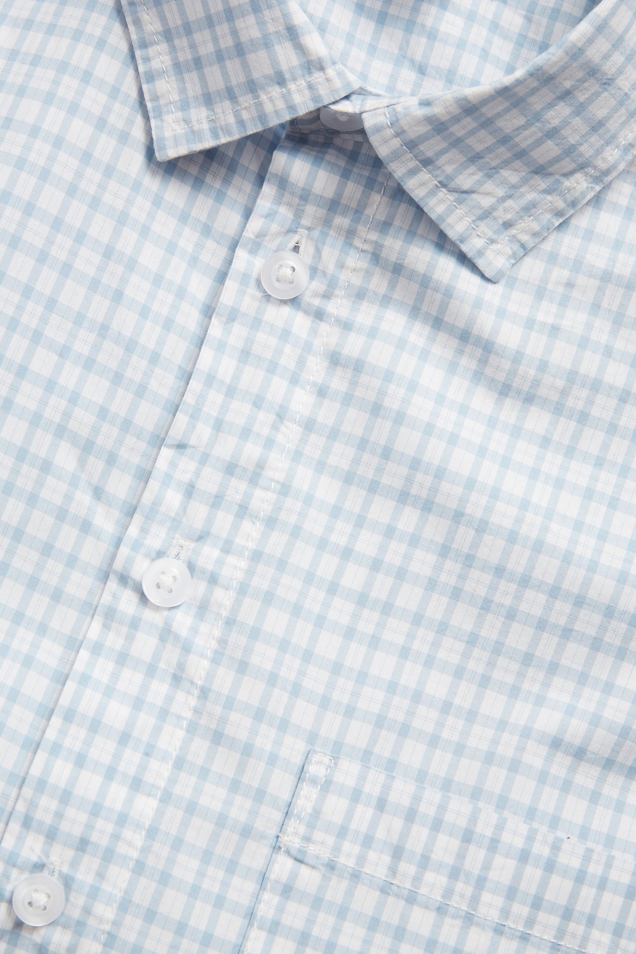 Närbild av en blå- och vitrutig kortärmad herrskjorta i bomull med krage, knappar och bröstficka.