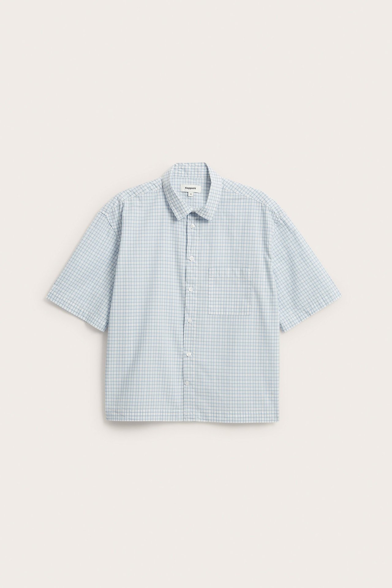 Framsida av en ljusblå rutig kortärmad skjorta i bomullspoplin med bröstficka och vita knappar.