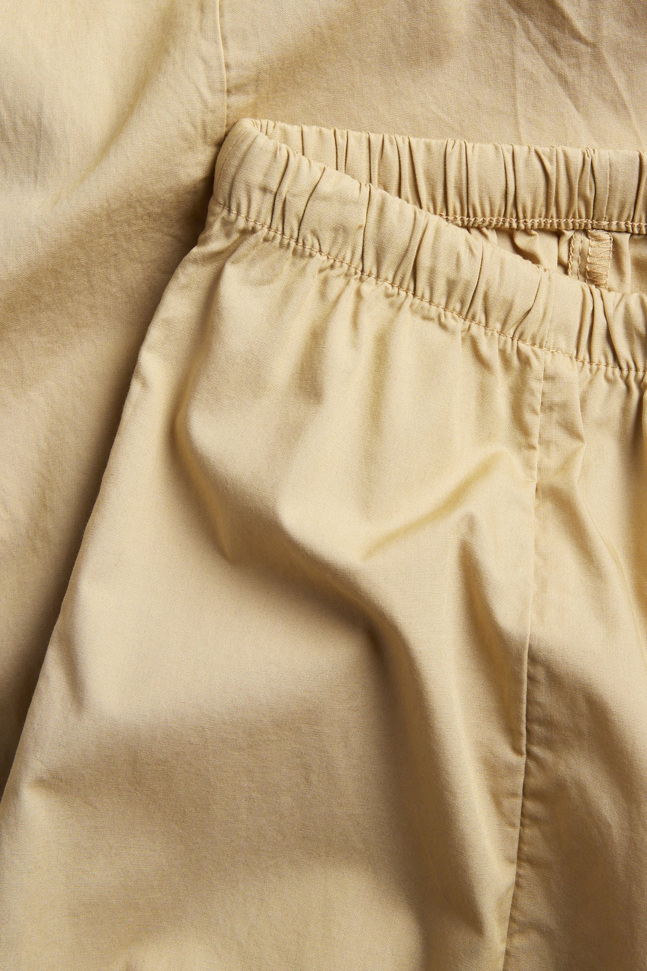 Lähikuva beigestä puuvillapopliinista ballongihousuista, joissa joustava vyötärö ja kiristysnyöri.