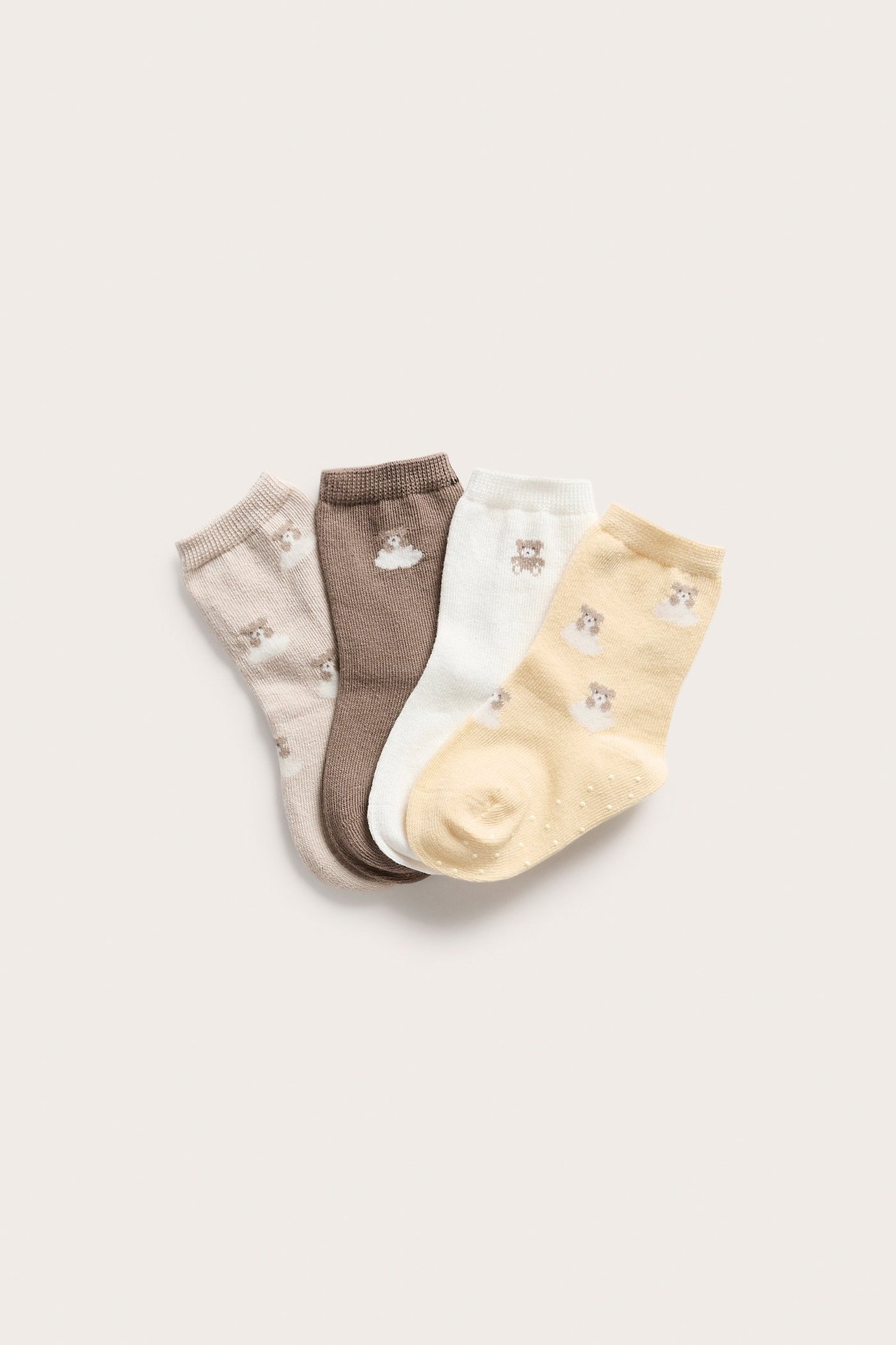 Fyra par babysockor: beige, brun, vit, gul. Med nallebjörnar, moln och halkskyddsprickar.