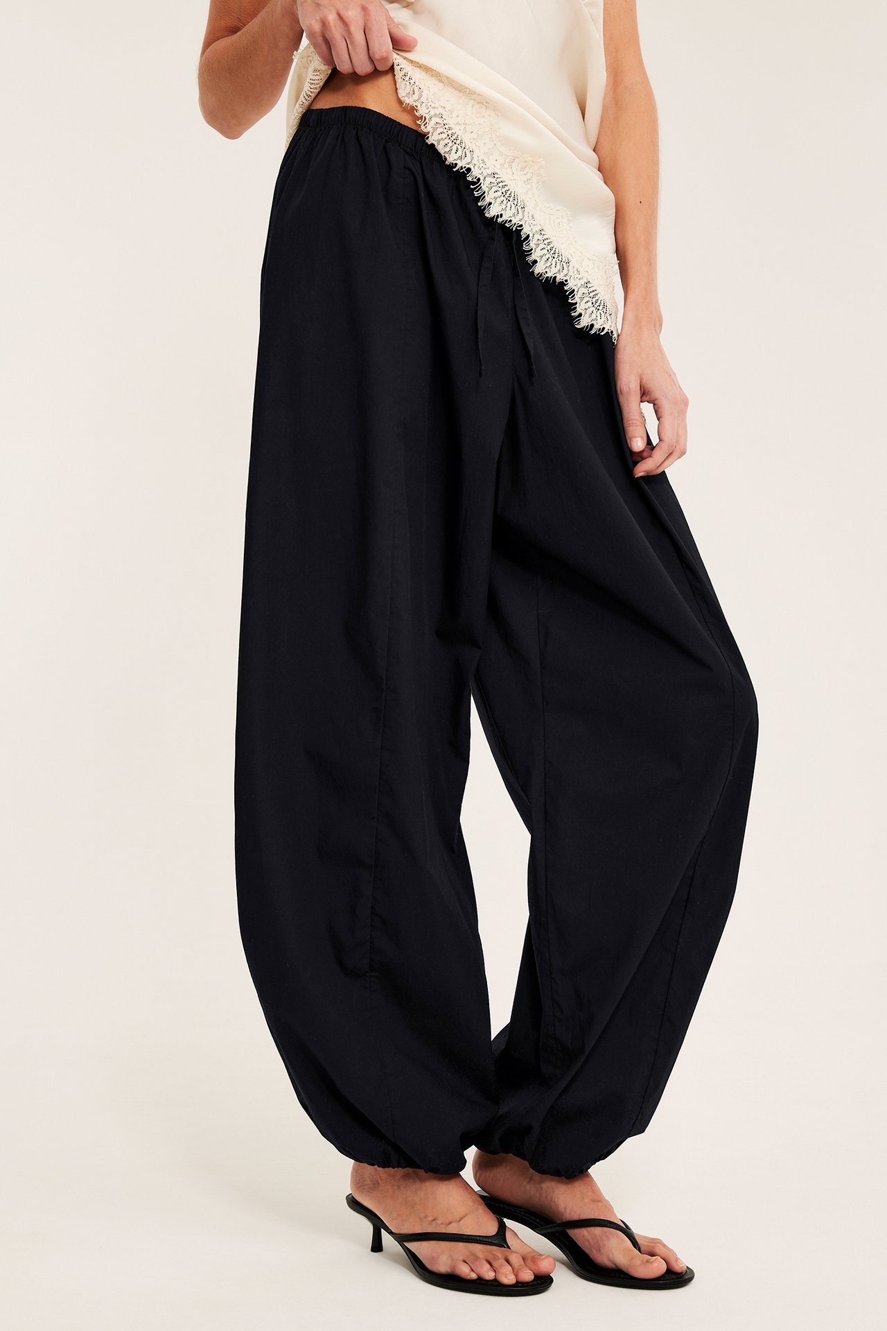 Sidovy: Kvinna bär svarta ballongbyxor i bomullspoplin, en krämvit spetstopp och svarta sandaler med klack.