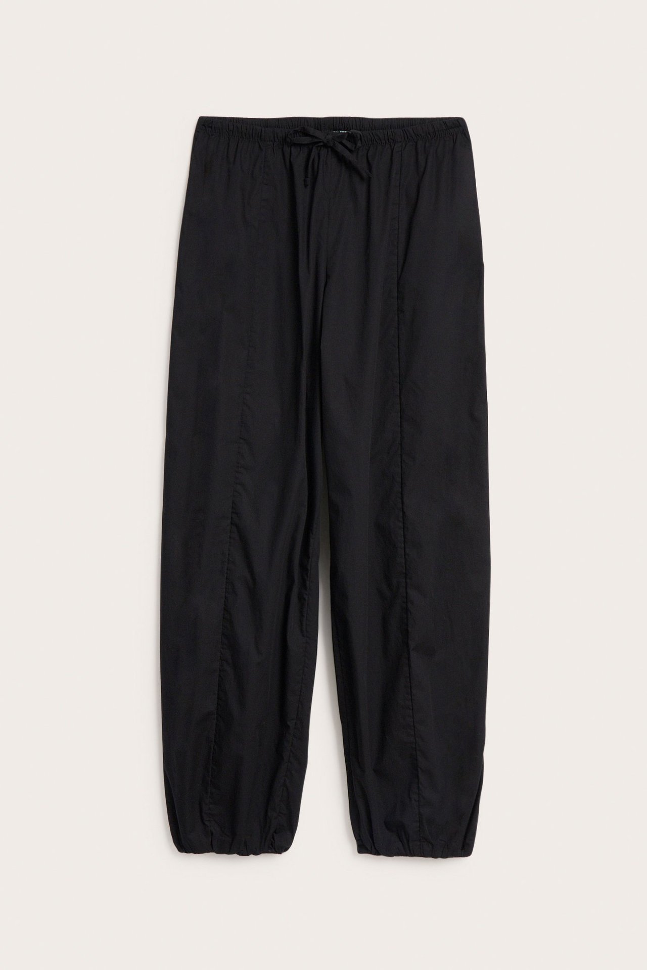 Framifrån, svarta ballongbyxor i bomullspoplin med elastisk dragsko i midjan och resår i benslut.