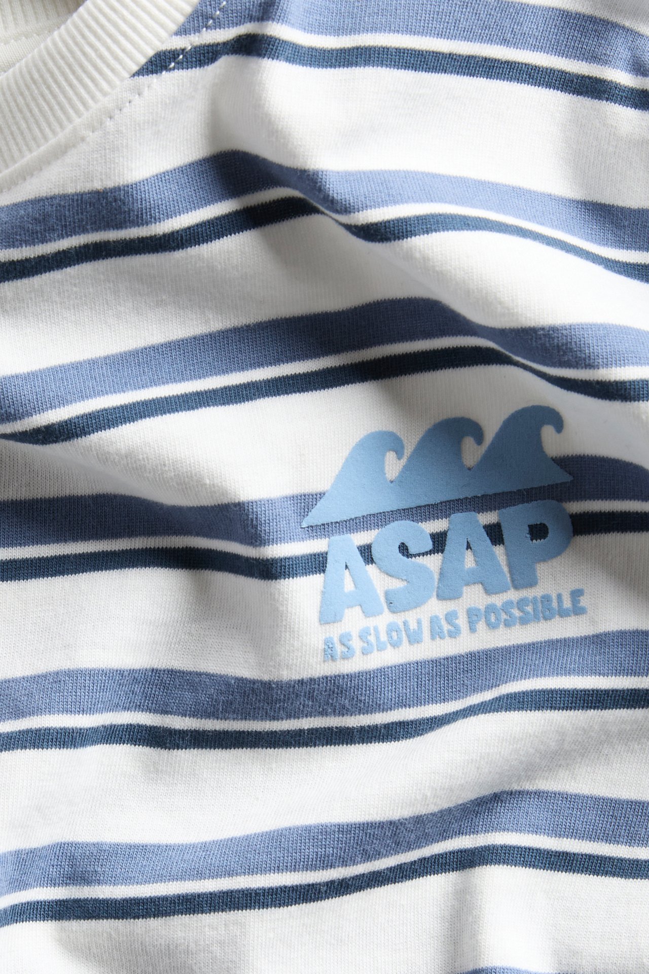 Zbliżenie na białą bawełnianą koszulkę w niebieskie paski z haftem 'ASAP' na piersi.