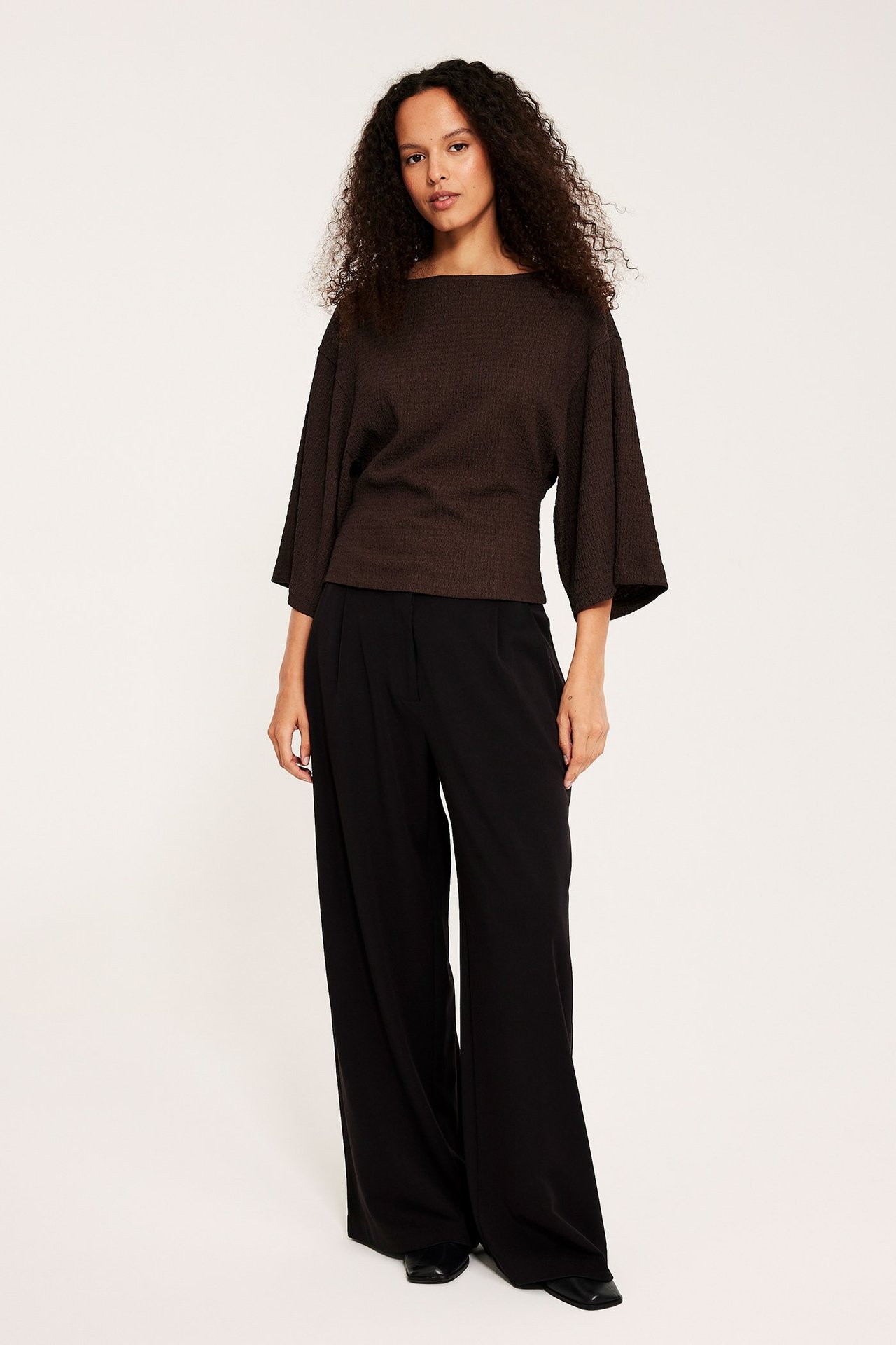 Widok z przodu: Kobieta w ciemnobrązowym topie kimono, czarnych spodniach i butach.