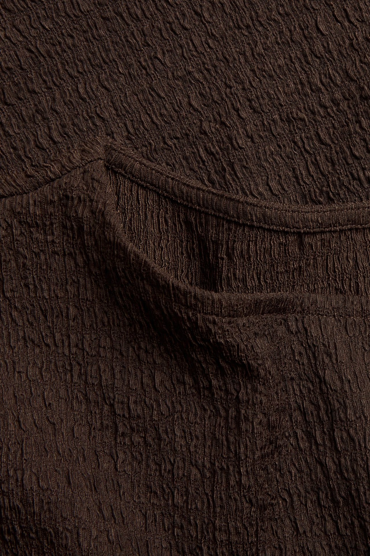 Zbliżenie ciemnobrązowego strukturalnego topu, ukazujące delikatny wzór fal tkaniny.
