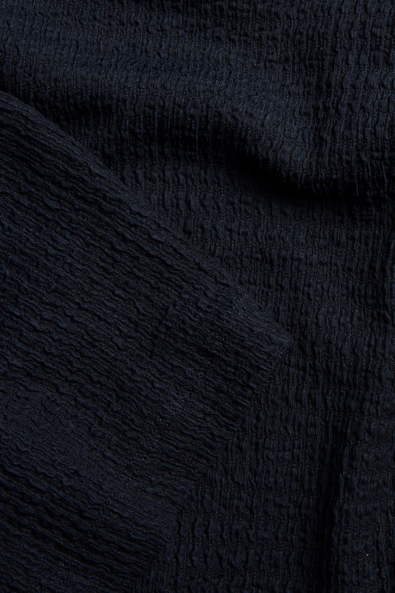 Zbliżenie na ciemnoniebieską, strukturalną tkaninę topu.