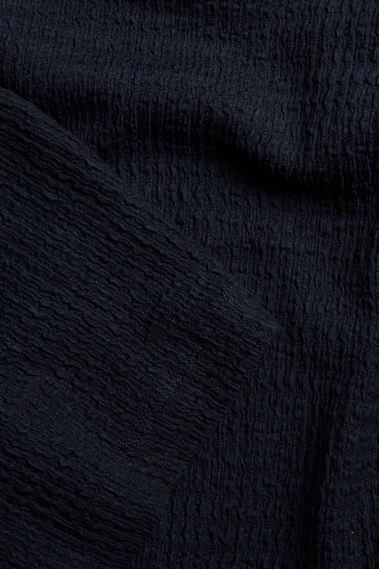 Zbliżenie na ciemnoniebieską, strukturalną tkaninę topu.