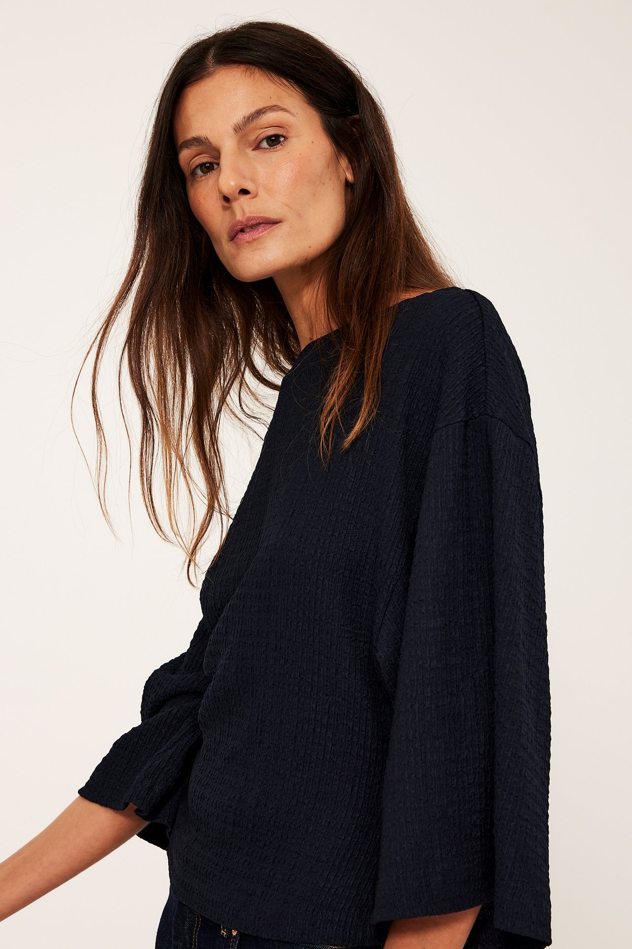 Framsidesvy av kvinna i mörkblå strukturerad topp med vida kimonosärmar.