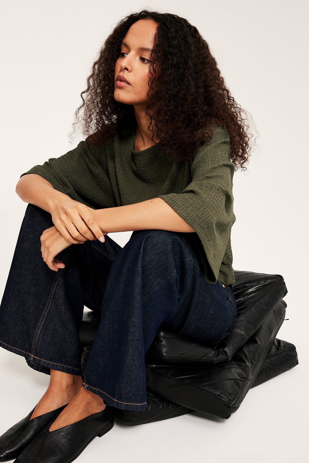 Nainen vihreässä strukturoidussa topissa leveillä kimono-hihoilla, tummansinisissä farkuissa, mustissa kengissä.