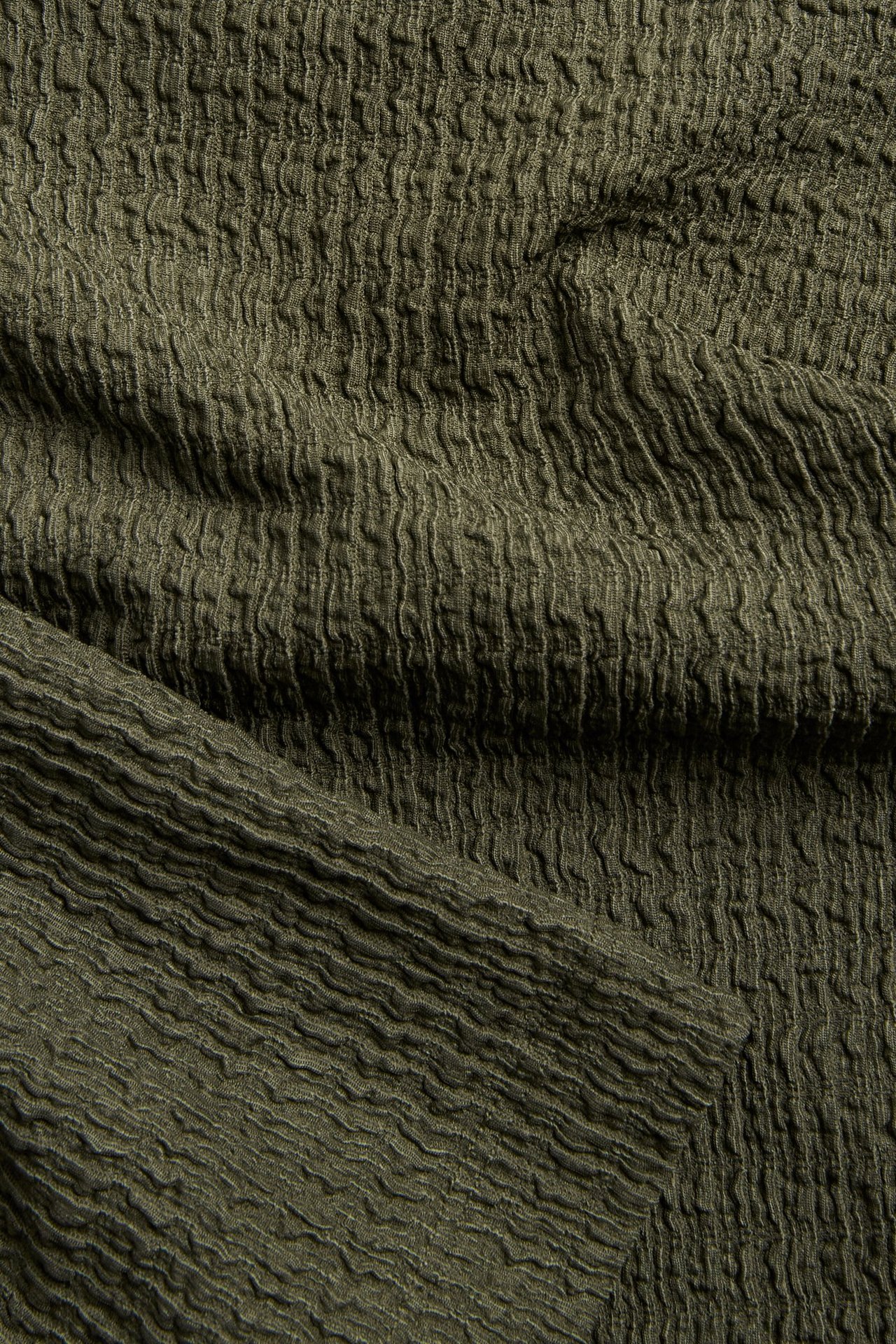 Zbliżenie na zielony, strukturalny materiał poliestrowo-elastanowy topu.