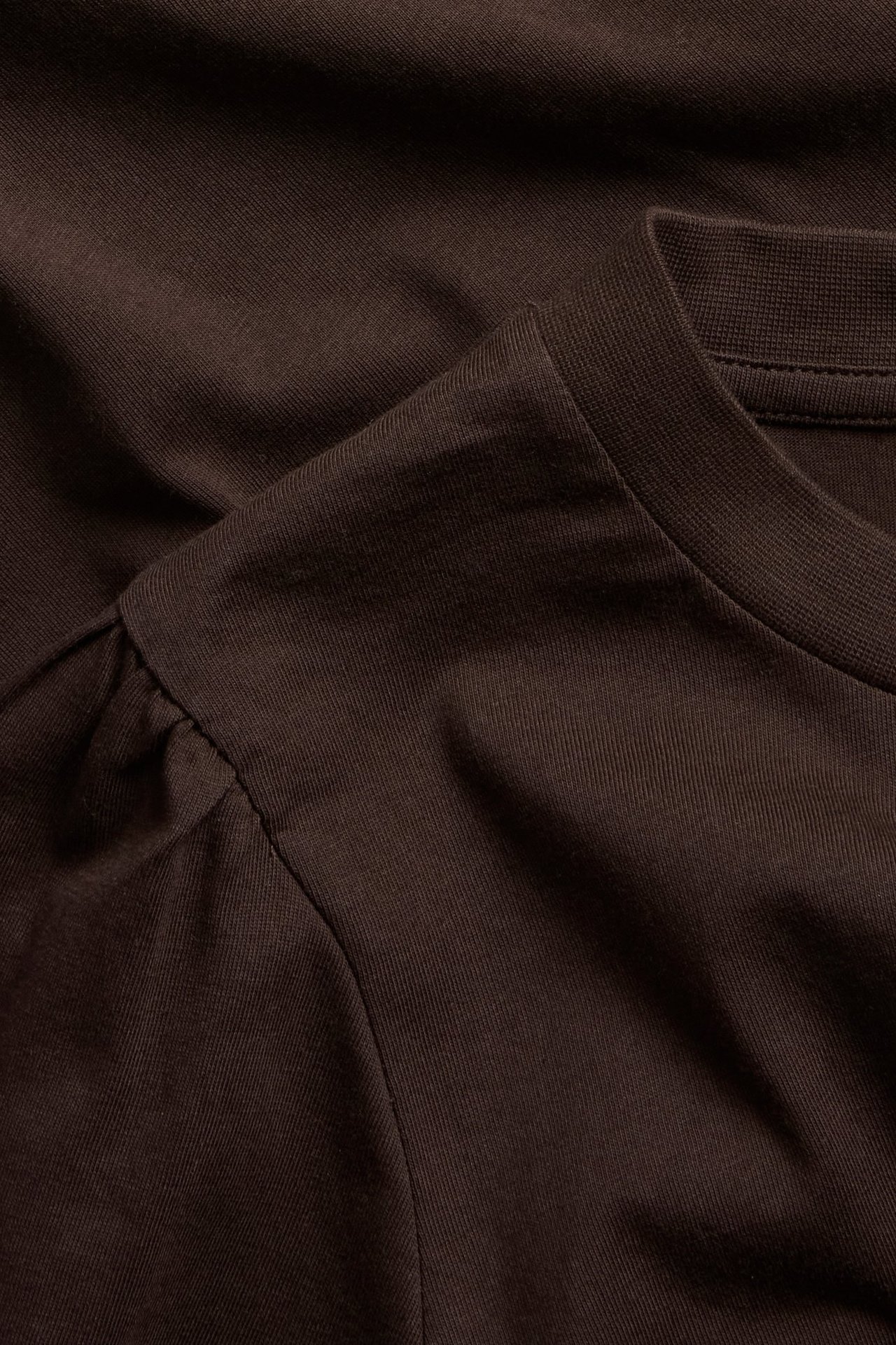 Nærbilde av en mørkebrun bomullstopp med puffermer og rund hals.