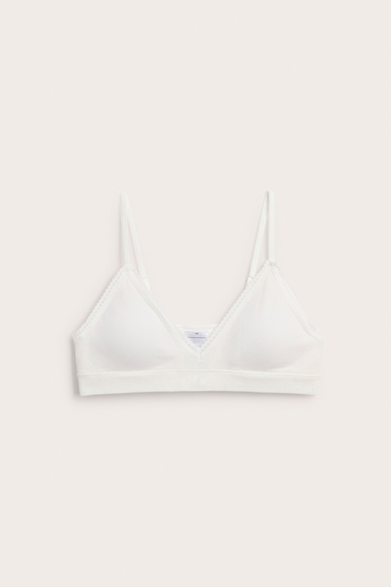 Framifrån, en offwhite vadderad sömlös kort topp med delikat spetskant och ribbad nederkant.