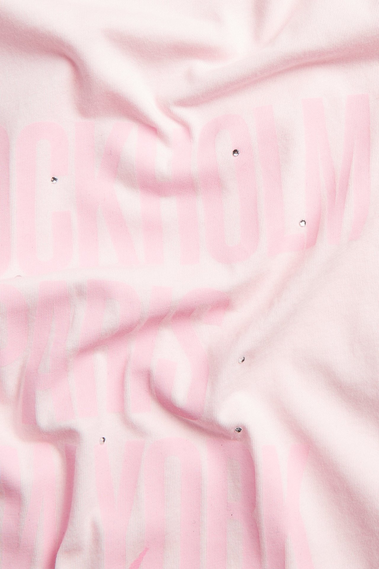 Zbliżenie na jasnoróżową bawełnianą koszulkę z różowym nadrukiem i rozsypanymi dżetami.