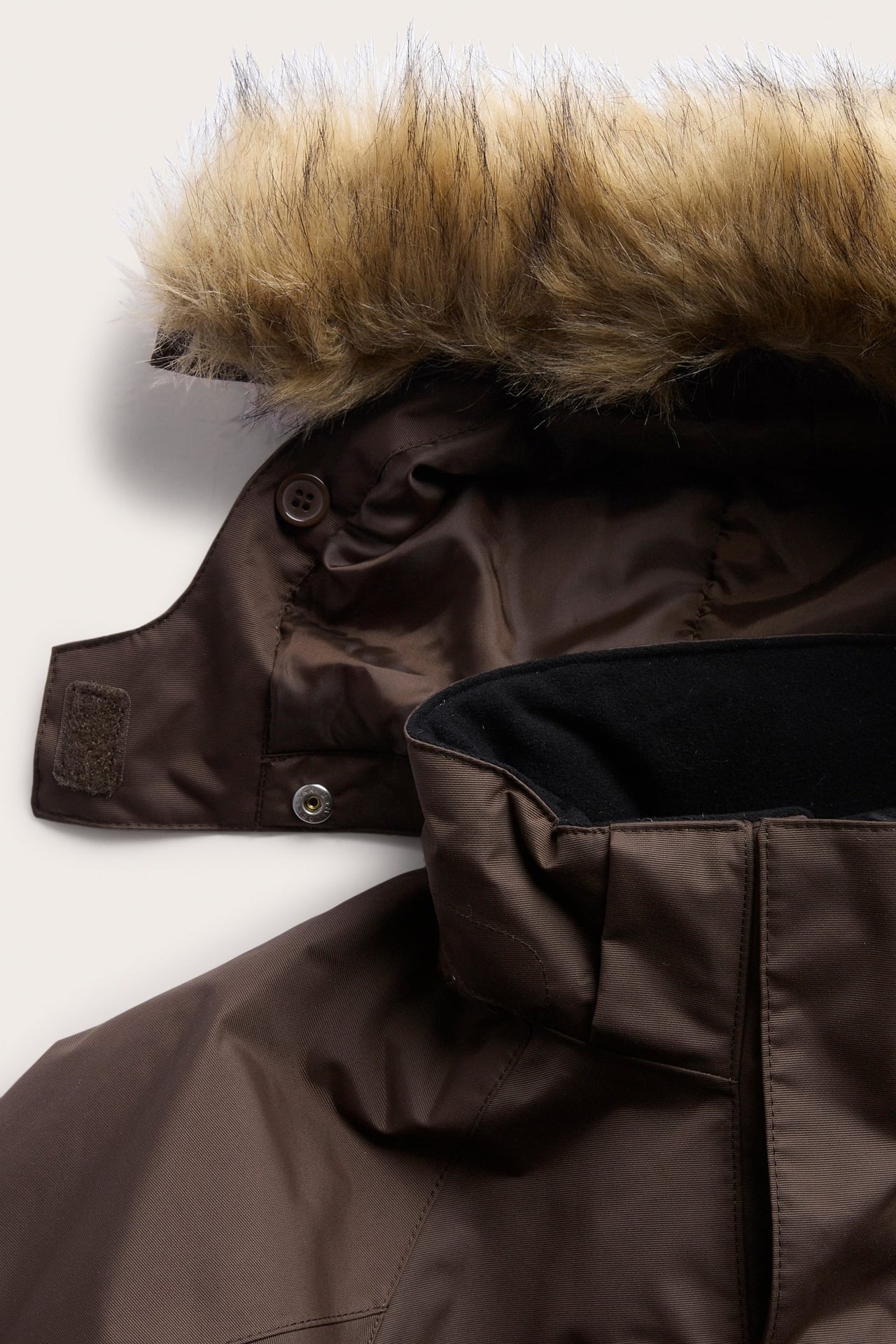 Nærbilde av en brun parka med fuskepelsfôret hette og svart fleecekrage.