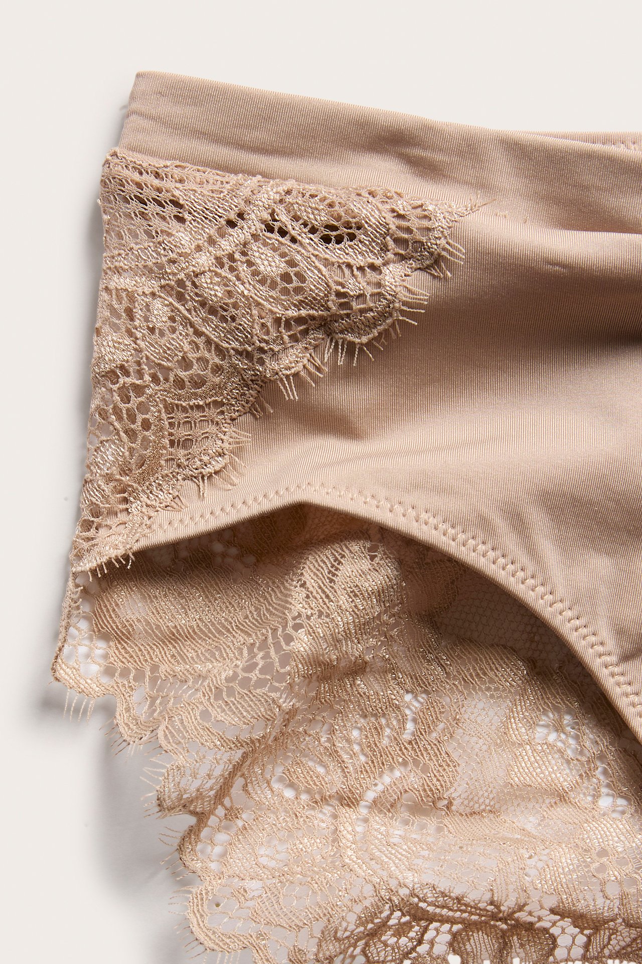 Nærbilde av beige mikrotruse med delikate blondedetaljer.