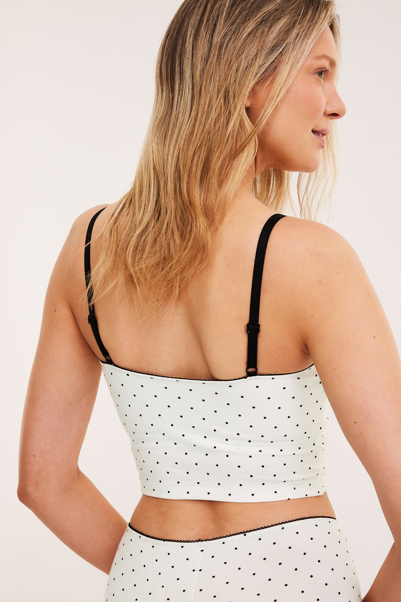 Ryggvy av kvinna i offwhite prickig bralette med svart picotkant och matchande trosa.