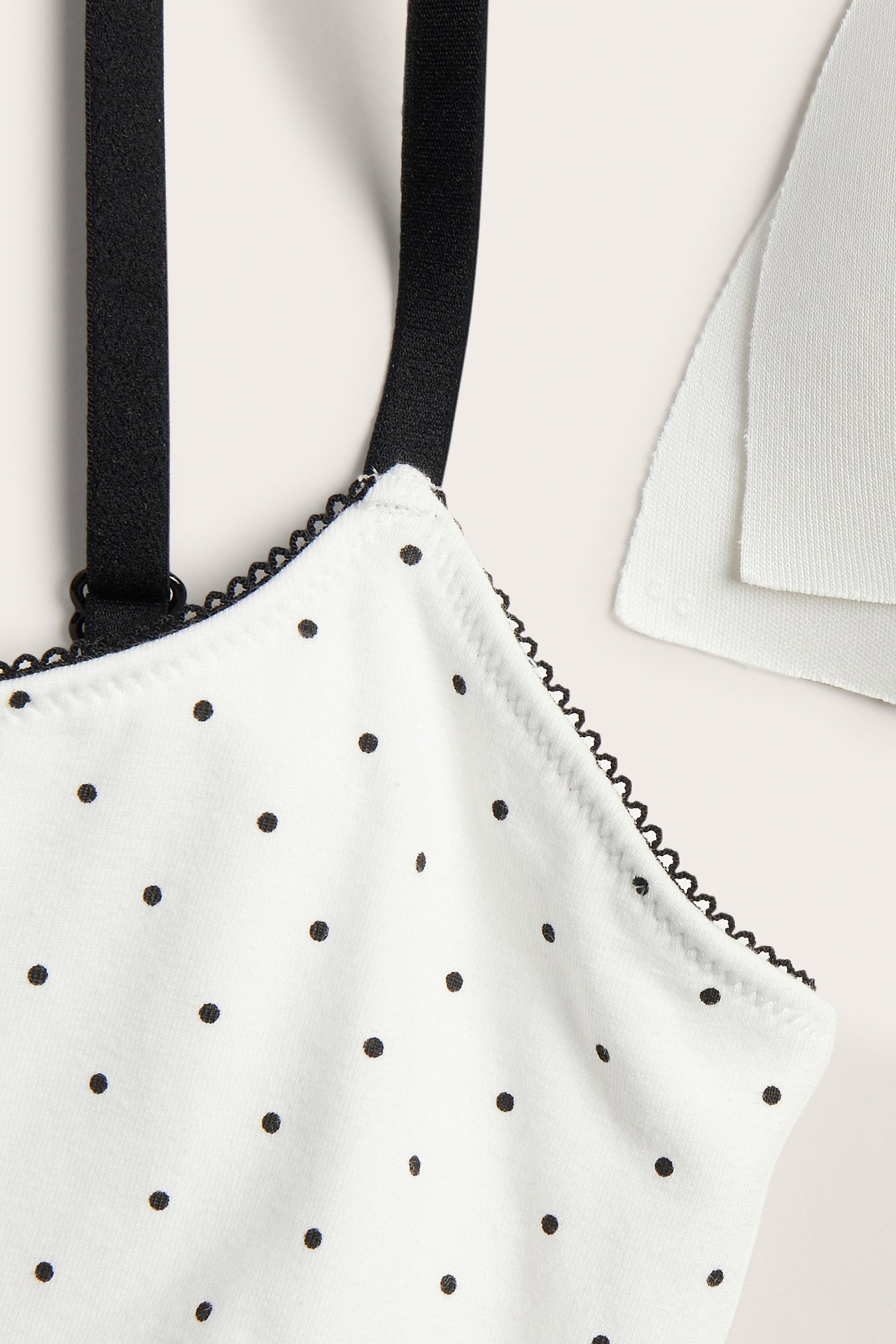 Närbild framifrån på en offwhite prickig bh-topp med svart picotkant och svarta axelband.