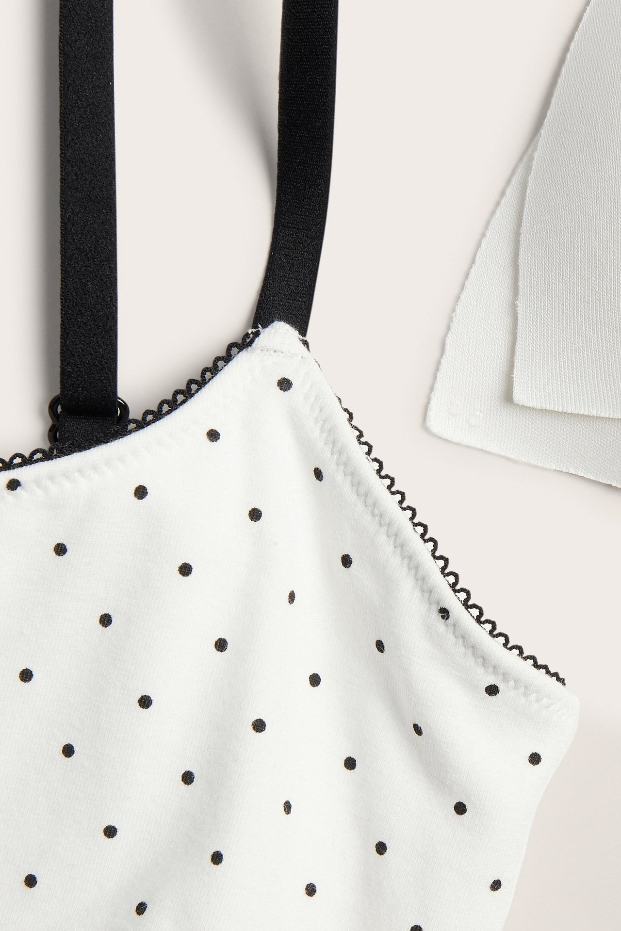 Närbild framifrån på en offwhite prickig bh-topp med svart picotkant och svarta axelband.