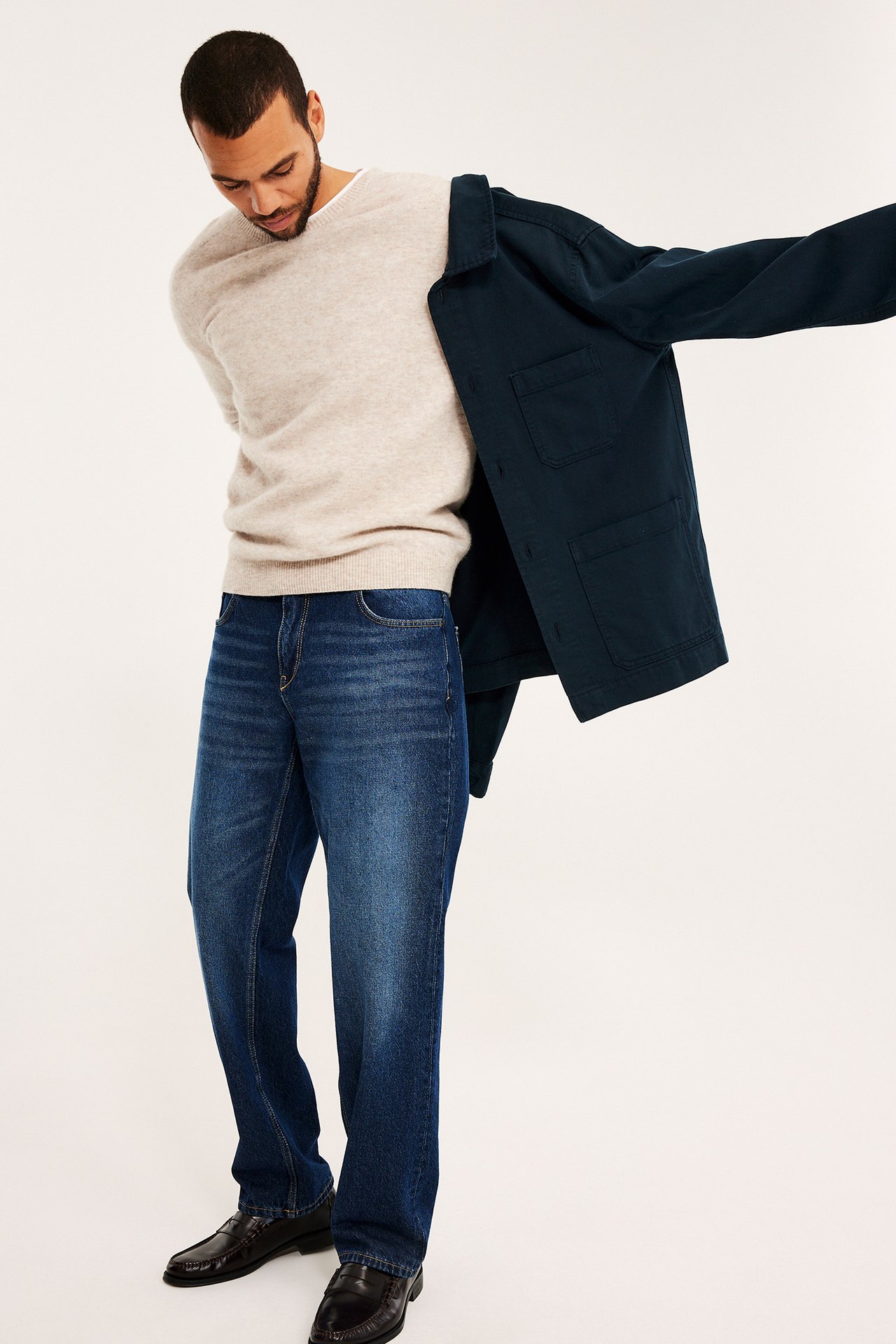 Mörkblå overshirt tas på över en beige tröja, blå jeans och bruna loafers.