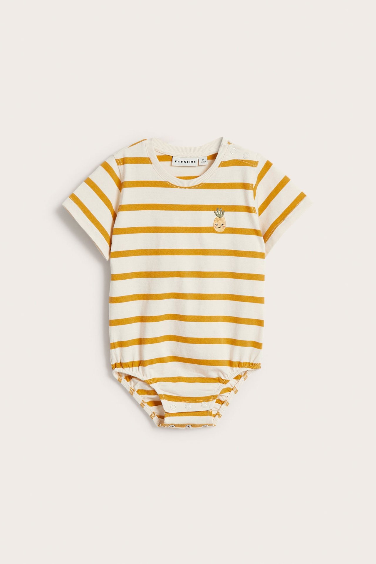 Forfra: kortermet babybody i kremfarget bomull med gule striper, ananasbroderi og trykknapper.