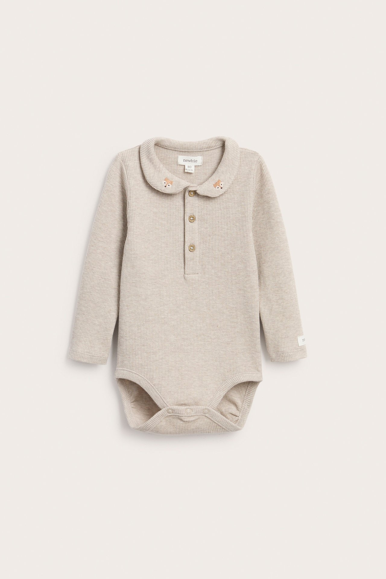 Framsida: beige ribbad långärmad babybody med broderad krage och knappslå.