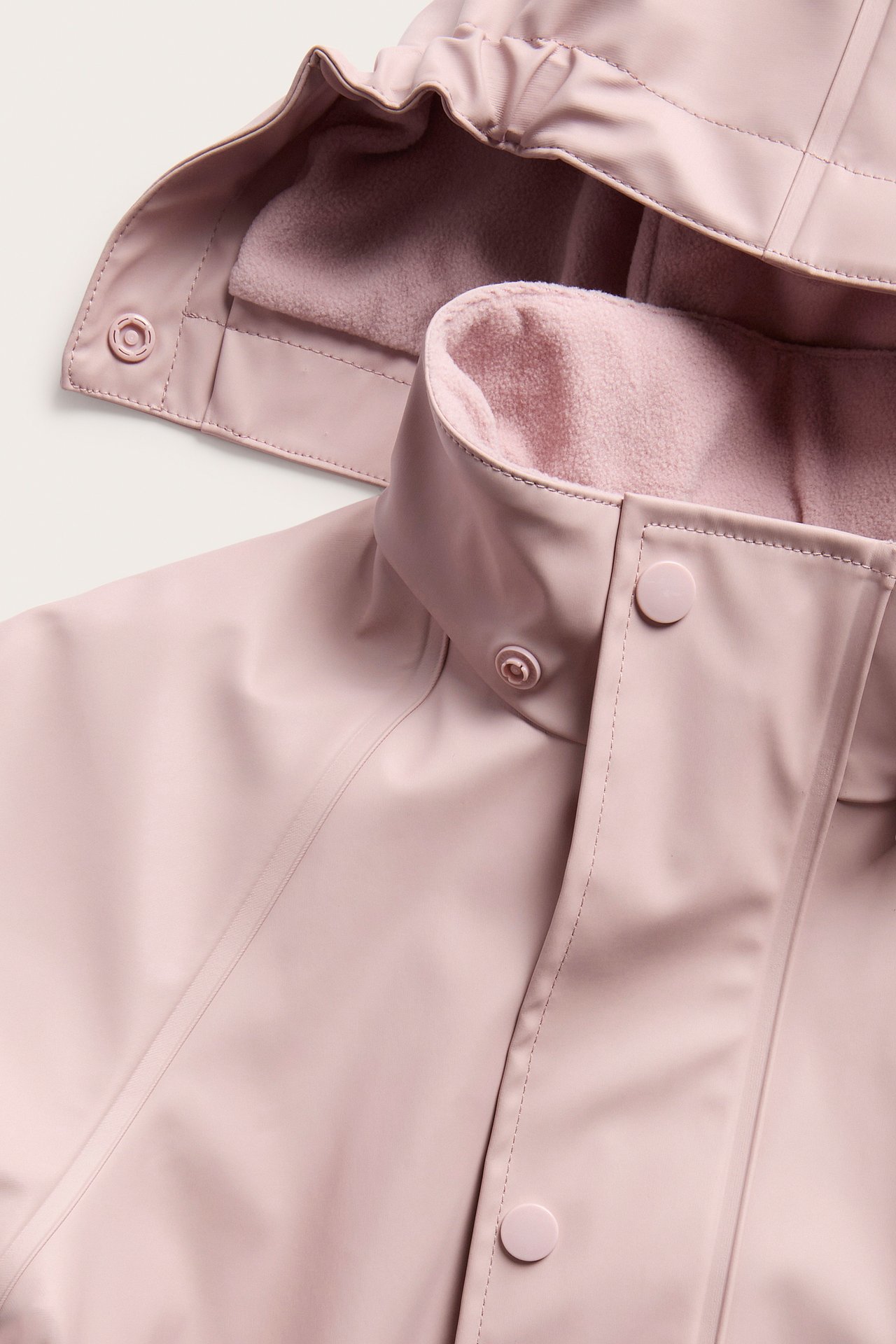Nærbilde av en rosa jakke med glatt yttermateriale, rosa fleecefôr og trykknapper.