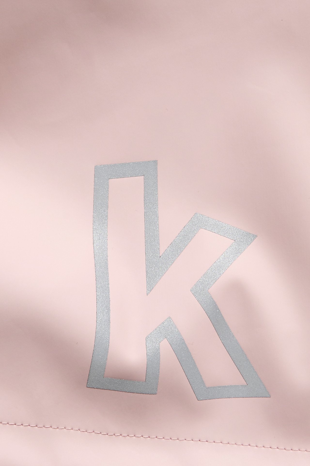Nærbilde av en lys rosa plaggdetalj med en sølvglitrende liten 'k' bokstav.